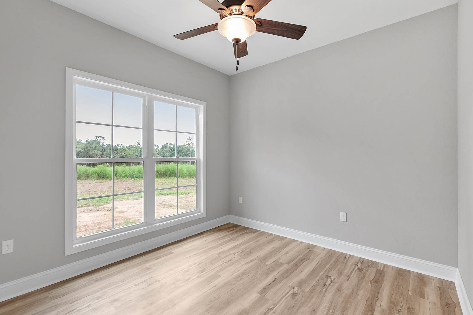 Ceiling fan with light fixture above wood flooring in a room featuring plaster walls and large windows overlooking a field