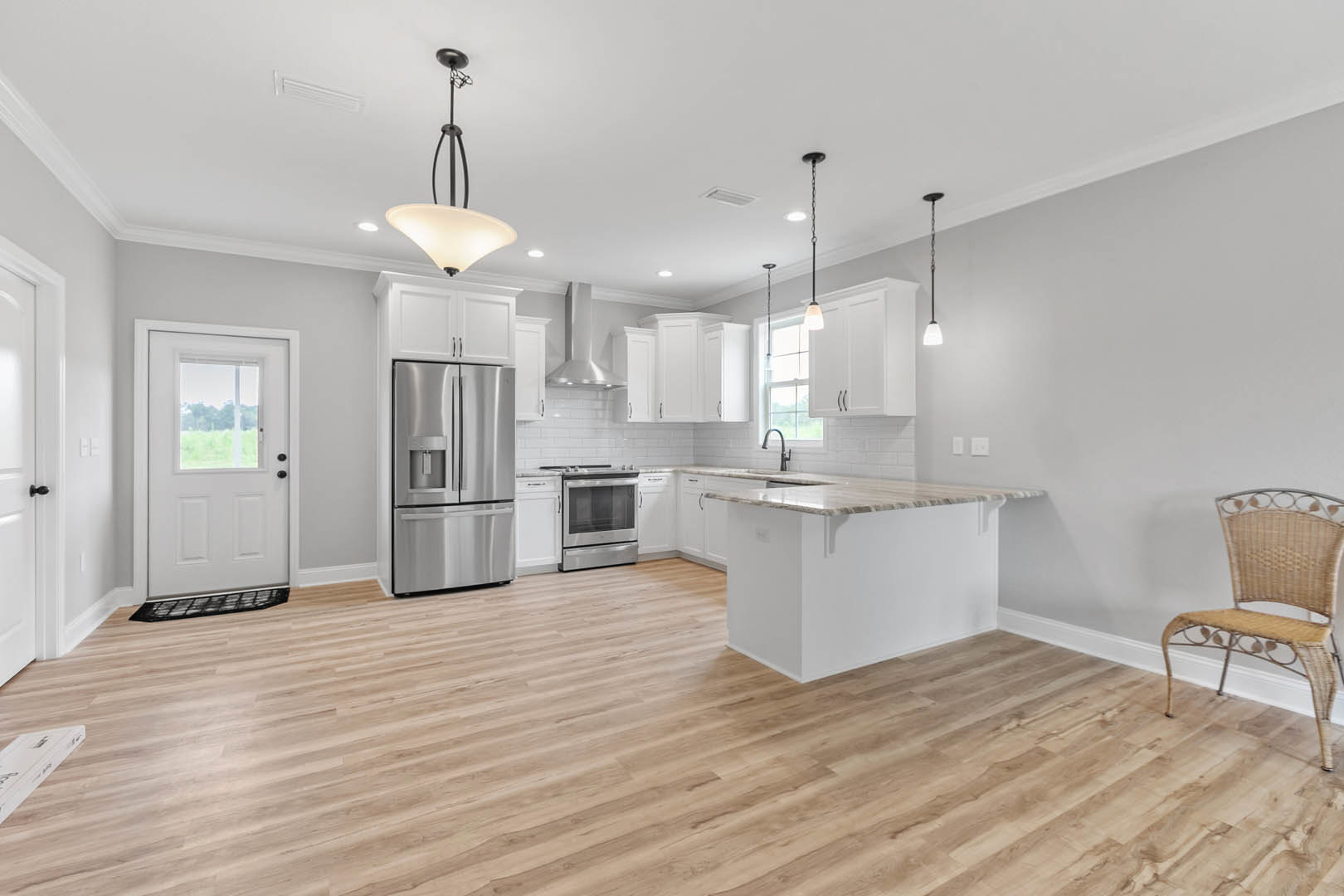 Kitchen with wood flooring, white shaker cabinets, stainless steel refrigerator, wicker chair, stove with metal finish, white door featuring glass window, modern pendant light
