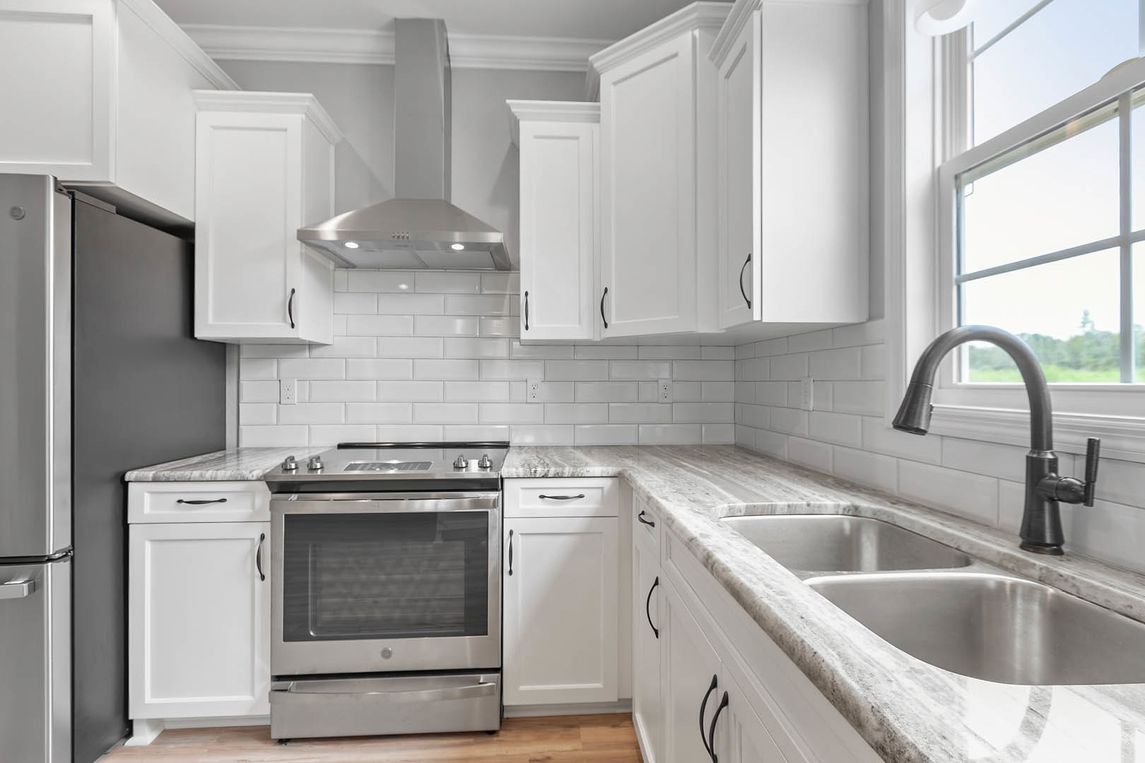 White cabinetry kitchen with stainless steel refrigerator, stove, microwave, and faucet, light countertops, and minimal decor