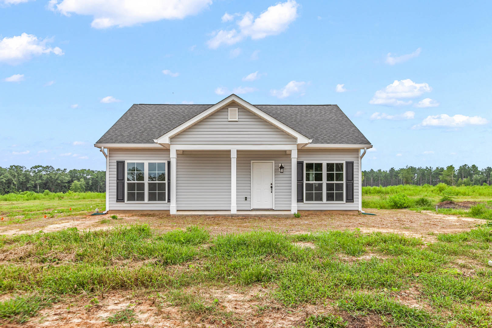 Two-story house with white front door, multi-pane windows, gray roof, and patch of green grass under a blue sky