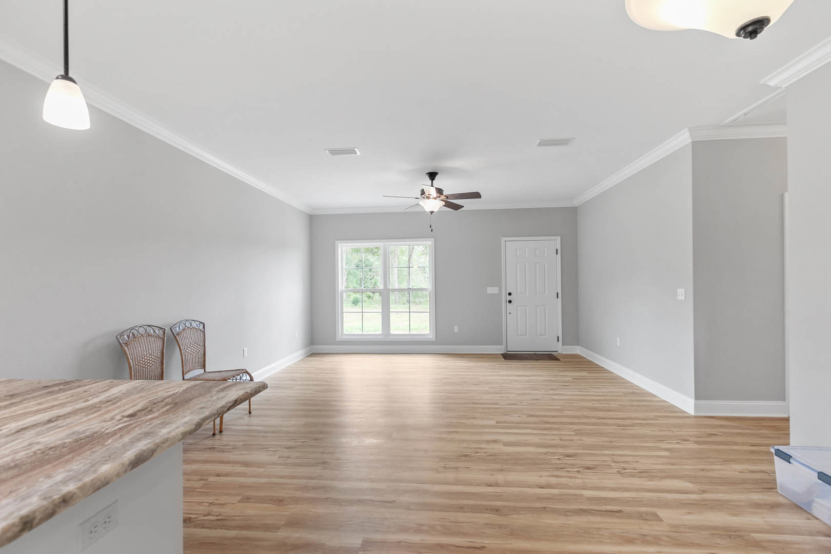 Dining area with wood table and upholstered chairs, multi-pane window, white door with black hardware, marble countertop, white-shaded pendant light, ceiling fan with integrated