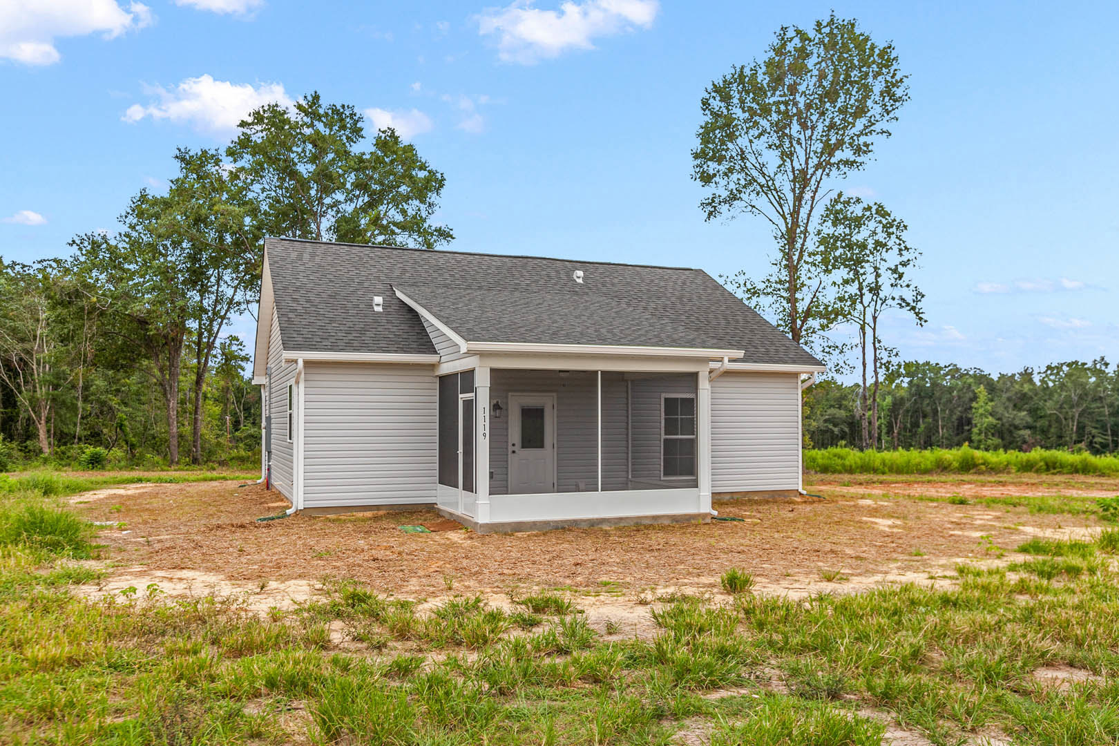 Two-story home with covered front porch, white framed door with window, surrounded by green grass lawn and mature trees under partly cloudy sky