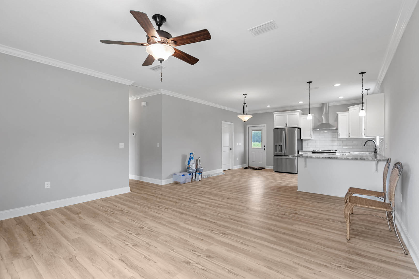 Living room with hardwood floors, ceiling fan with light fixture, wicker chairs, white doors including one with a window, and a stainless steel refrigerator visible in the