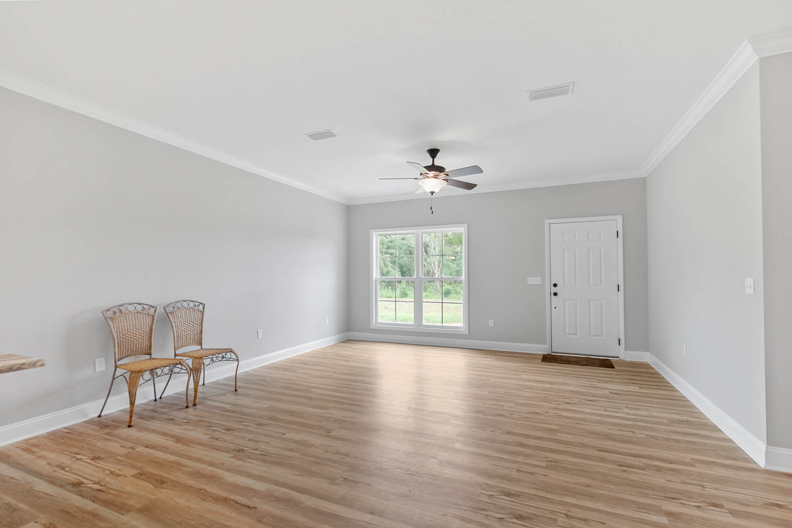 Hardwood floor room with two chairs, one wicker and one upholstered, white paneled door with black knobs, multi-pane window, ceiling fan, plaster walls