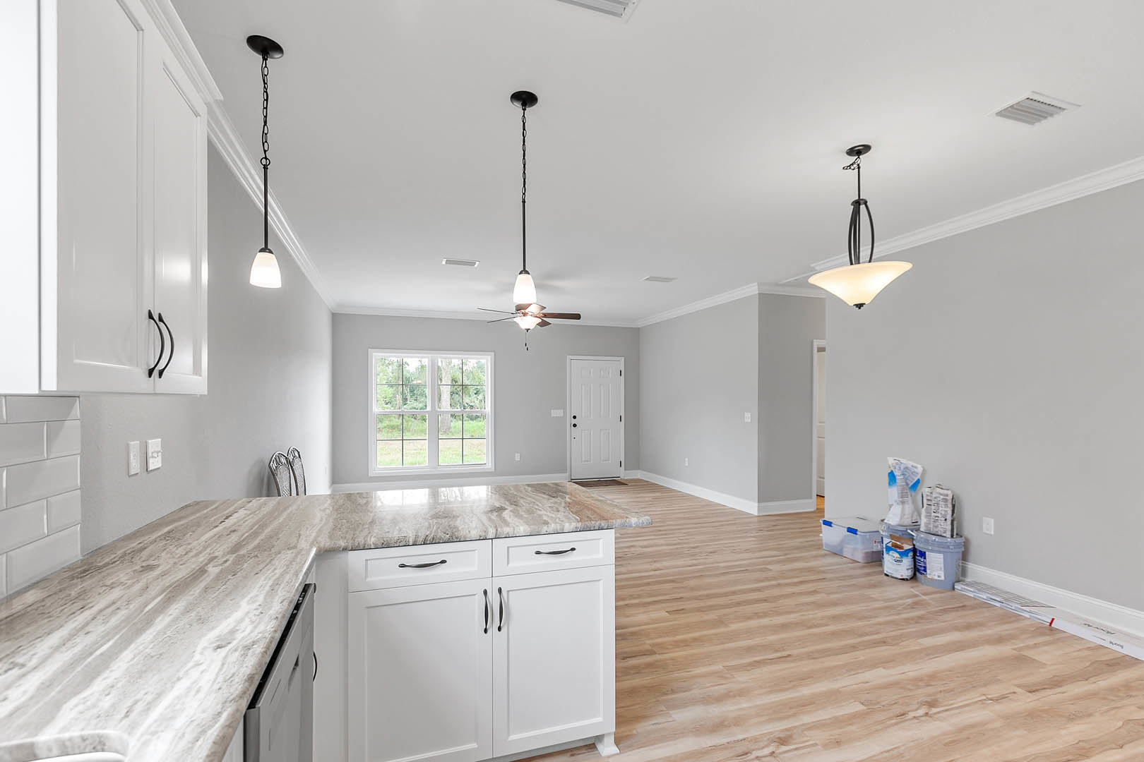 Marble countertop kitchen with hardwood flooring, multi-pane window, white door with black knobs, black metal curtain rod, ceiling light fixture, and cabinetry.