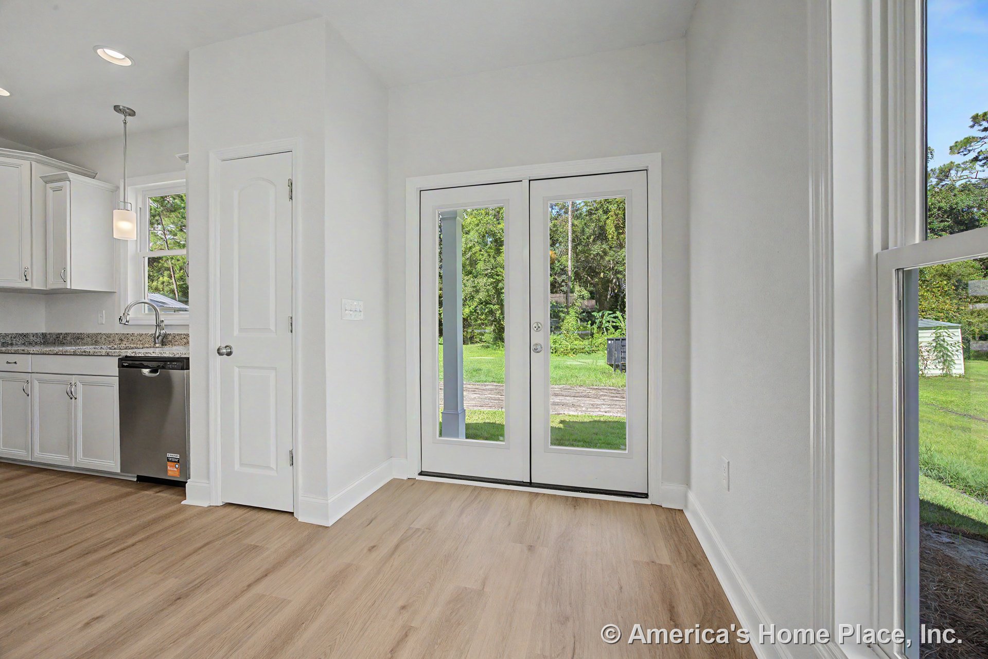 White kitchen cabinetry with granite countertops, stainless steel dishwasher, pendant light fixture above, light wood flooring, and double glass patio doors providing backyard