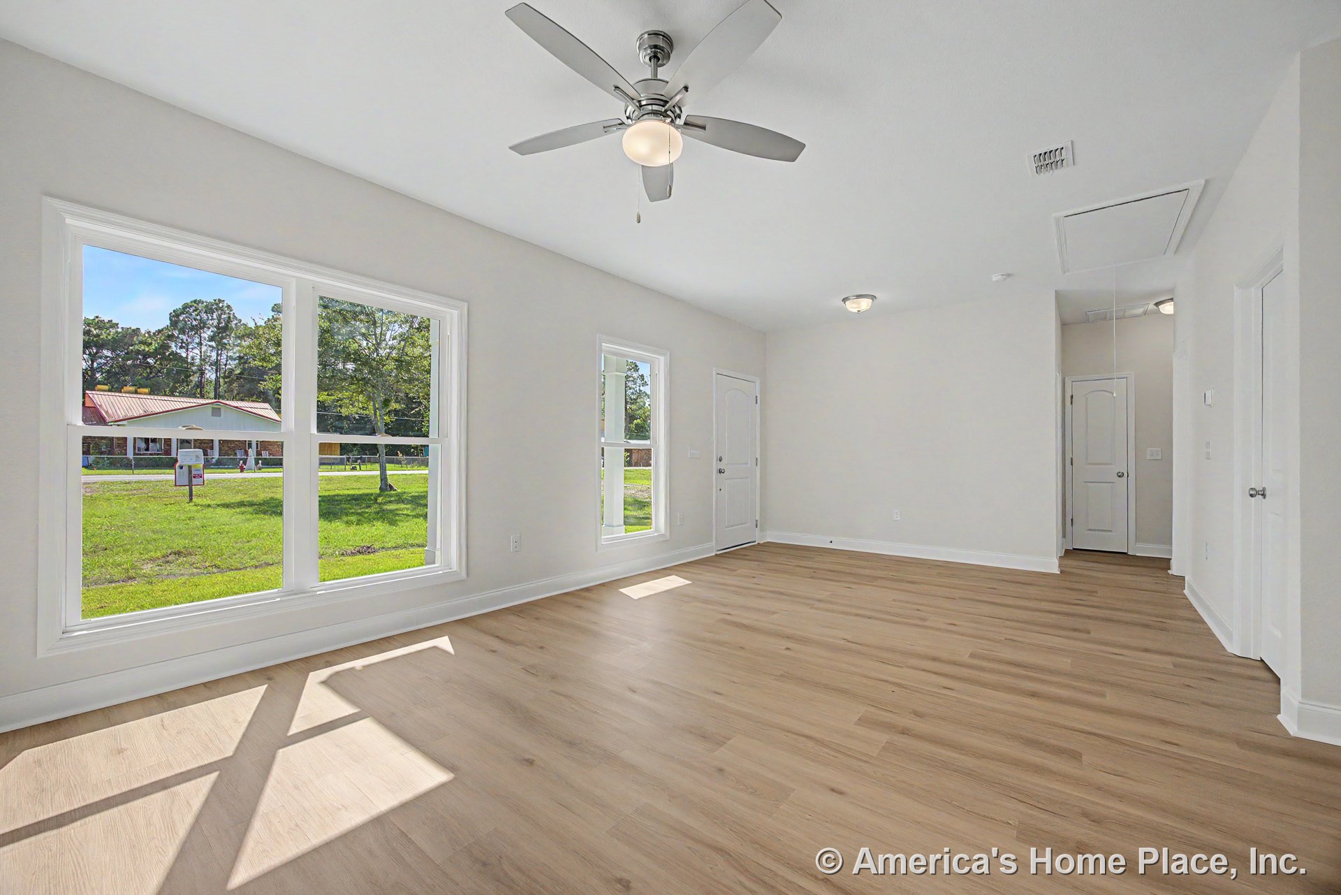 Living room with expansive picture windows, light wood plank flooring, white trim and baseboards, ceiling fan with integrated lighting, neutral wall color, and panel doors.