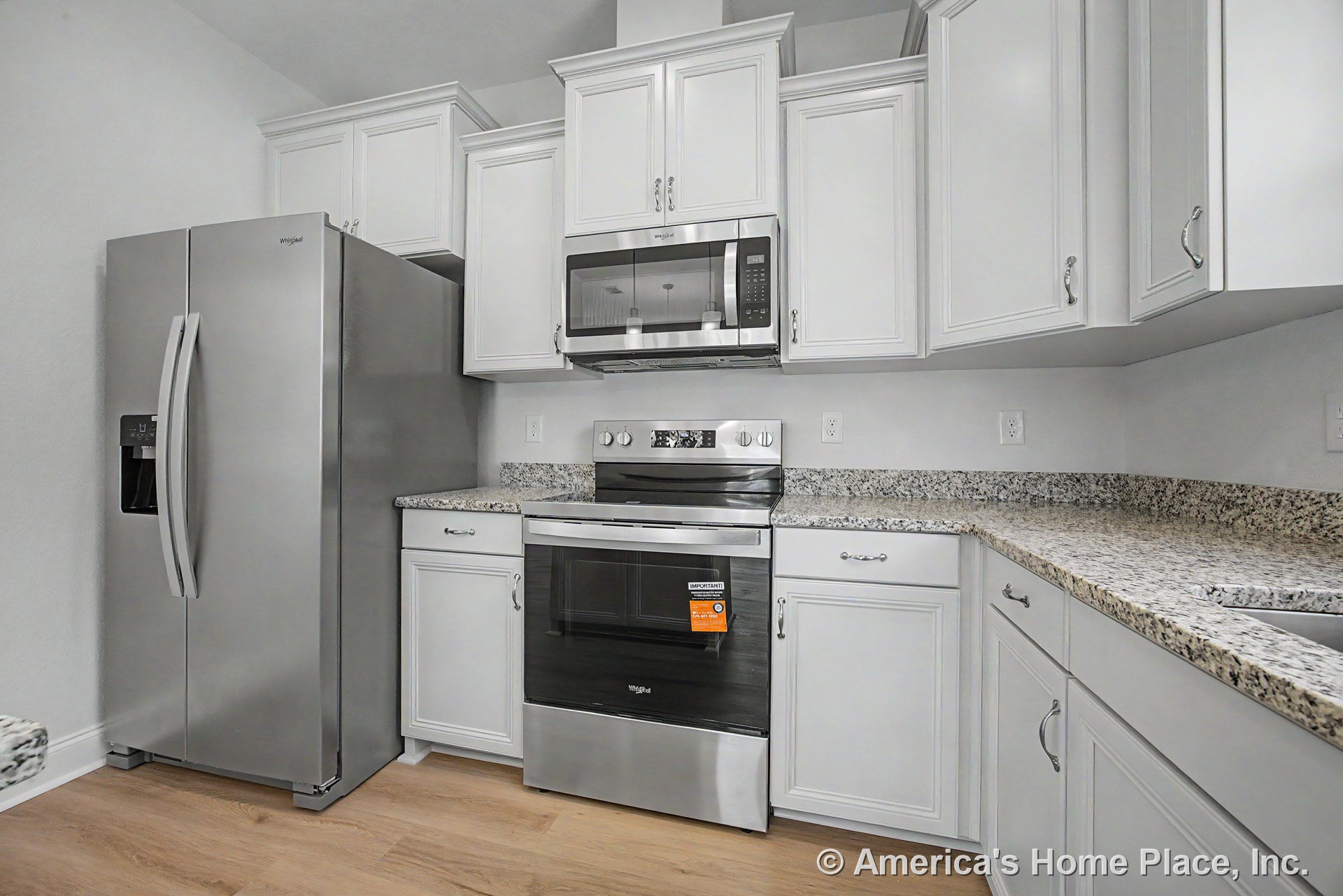 White upper and lower kitchen cabinets with built-in hardware, granite countertops, stainless steel refrigerator, oven, and microwave, light wood flooring.