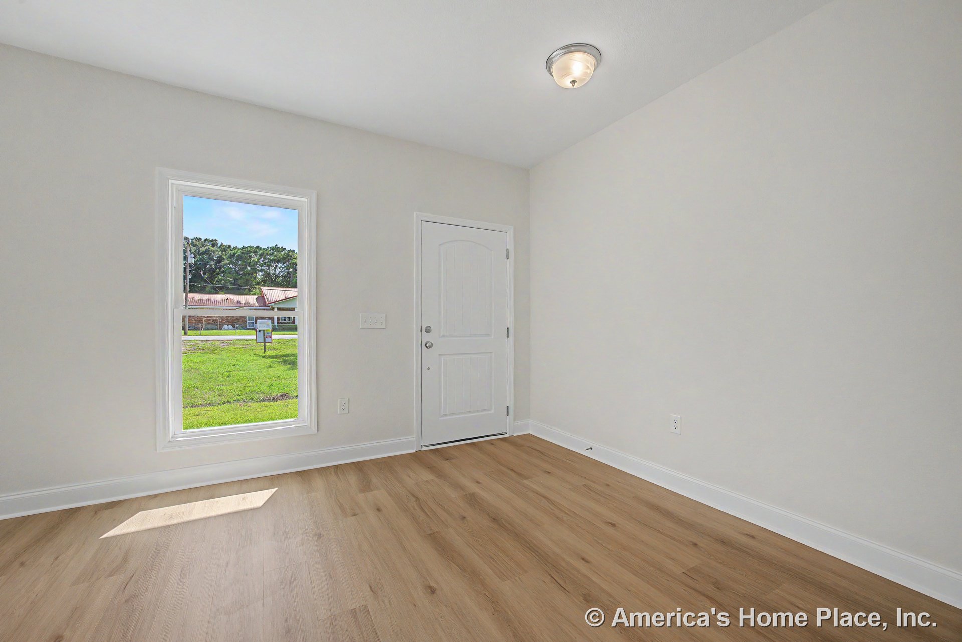 Paneled front door and large window with white trim in foyer, light wood plank flooring, flush mount ceiling light, white baseboards, and neutral walls.