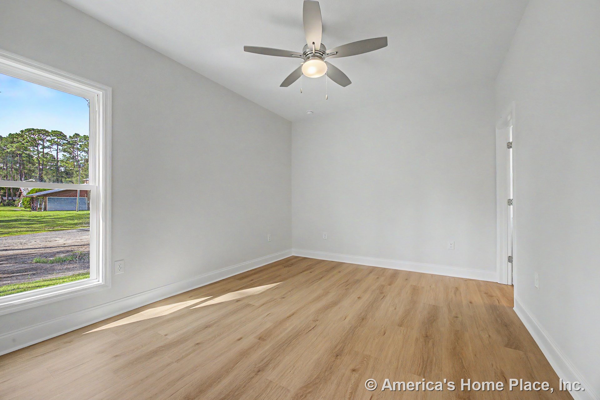 Bedroom with light wood plank flooring, white painted walls, large window with white trim, ceiling fan and built-in light fixture, baseboard trim, and hinged door with white