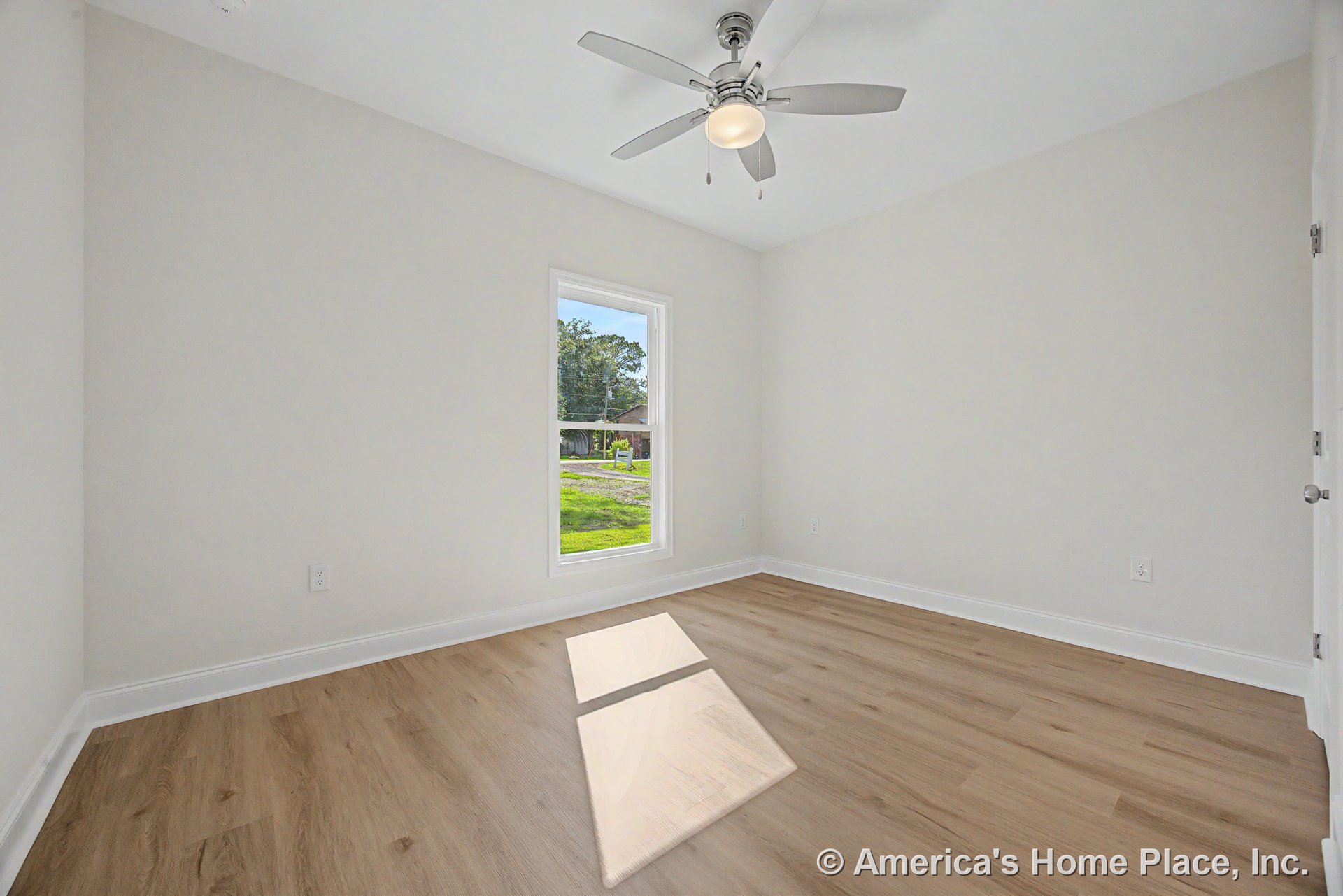 Bedroom with light wood plank flooring, white baseboards and trim, single window with white frame, ceiling fan and built-in light fixture, neutral wall color, standard interior