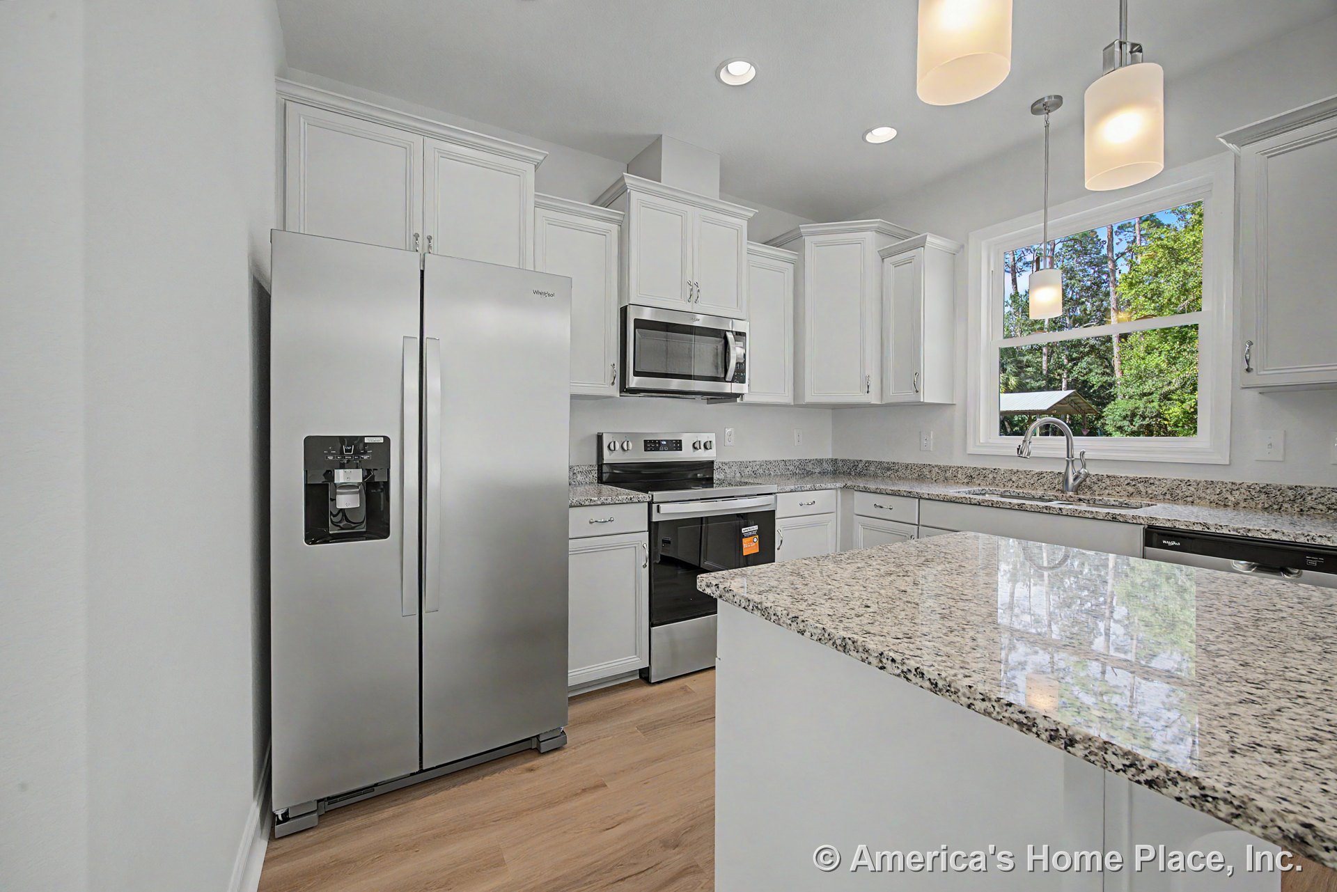 White upper and lower cabinets with granite countertop peninsula, stainless steel side-by-side refrigerator, built-in microwave and oven, electric range, dishwasher, large window