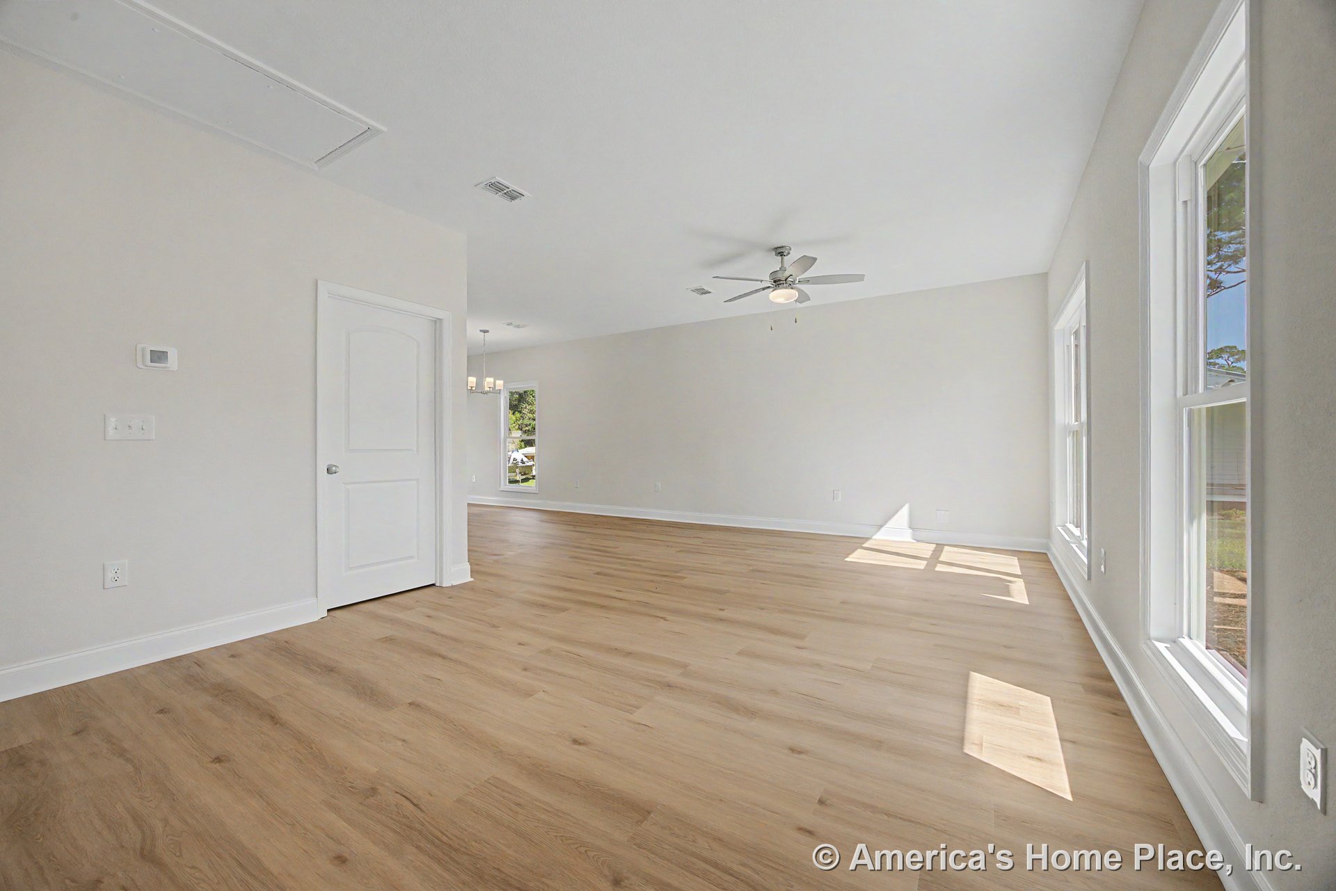 Light wood-look flooring, large double-hung windows with white trim, neutral painted walls, white baseboards, ceiling fan with integrated light fixture, paneled interior door, and