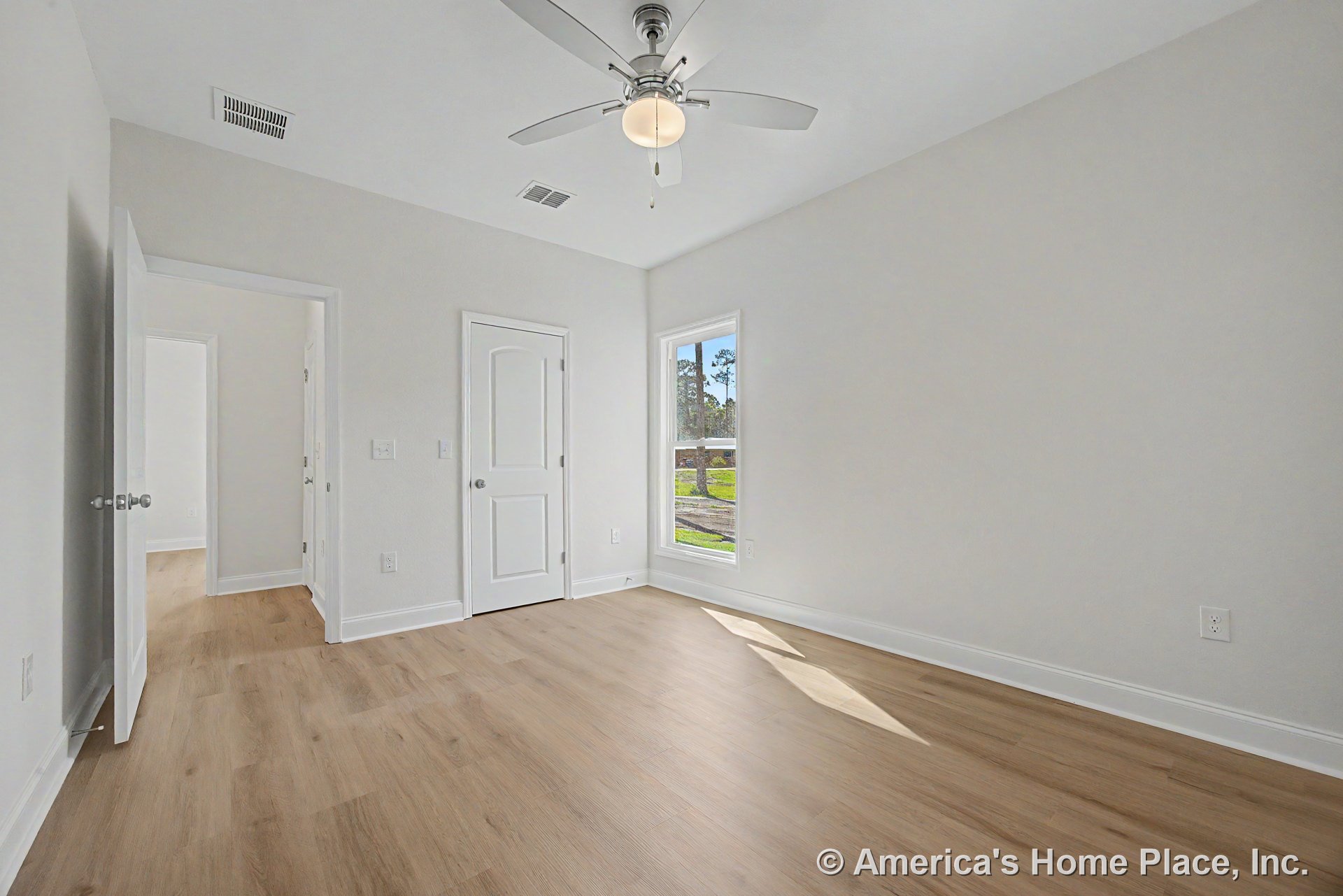 Bedroom with light wood plank flooring, white baseboards and trim, double panel doors, large window with white casing, ceiling fan featuring built-in light fixture, and neutral