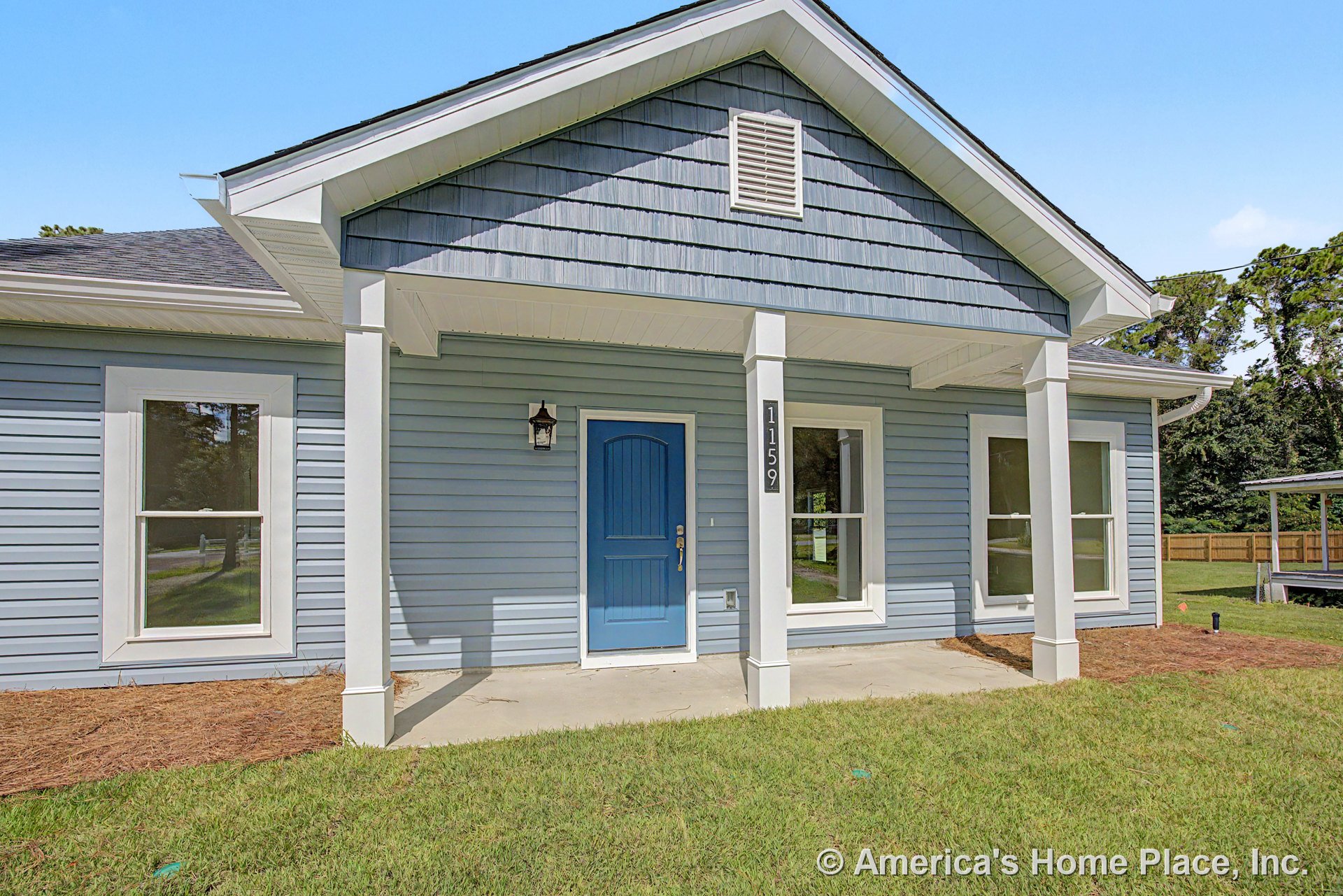 Covered front porch with blue horizontal lap siding, matching blue entry door, white trim windows, gable roof, exterior wall lantern, white columns, and concrete walkway.