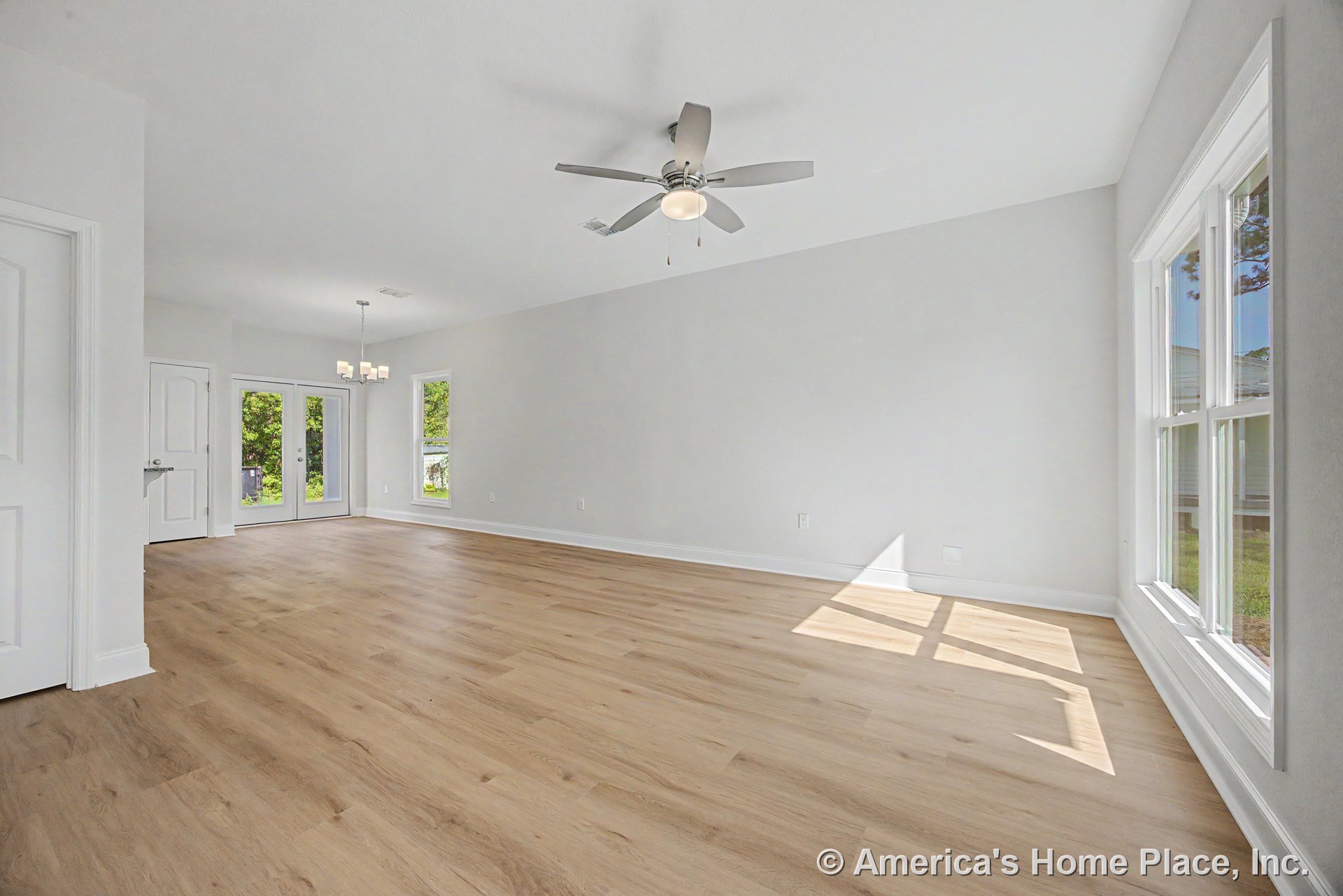 Open living area with light wood plank flooring, double window with white trim, ceiling fan with light, white walls and baseboards, glass doors leading outside, and modern