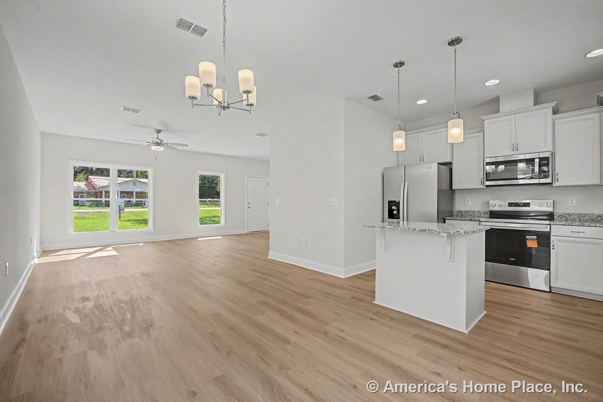 Open concept kitchen and living area with light wood flooring, white shaker cabinets, granite island, stainless steel appliances, large windows, pendant lights, chandelier, ceiling