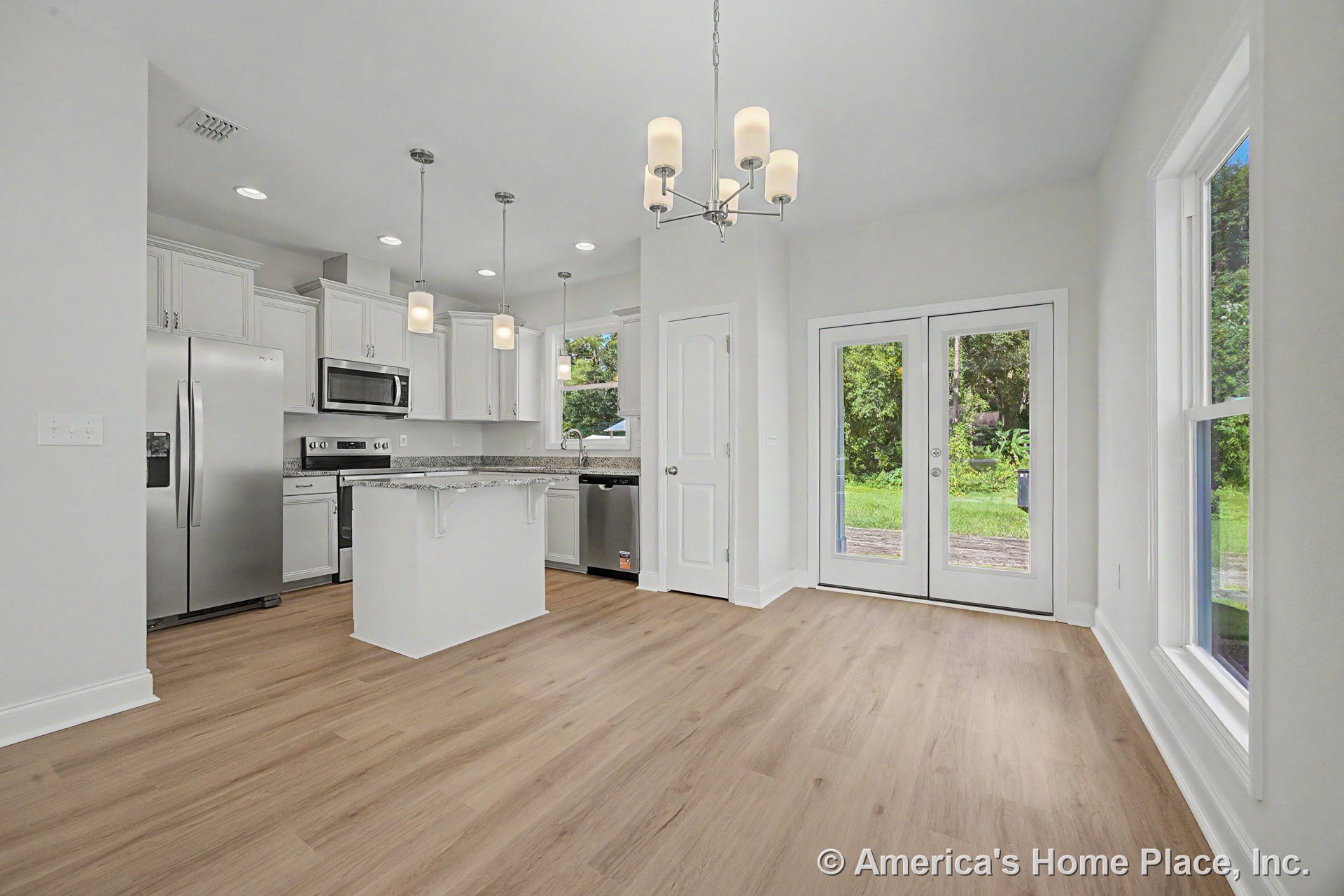 White shaker kitchen cabinets and granite island with pendant lighting, stainless steel appliances, light wood plank flooring, open dining area with chandelier, large windows, and