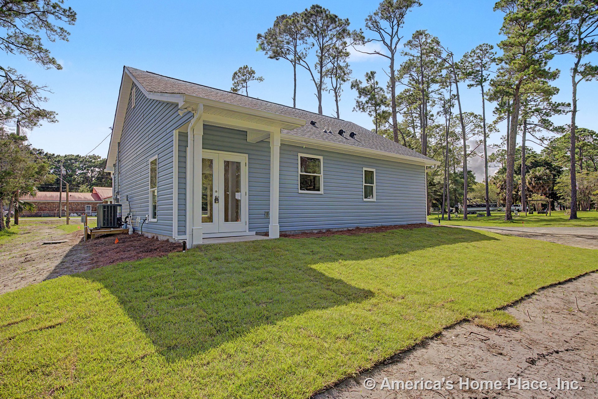 Blue horizontal siding with white trim, covered porch entry featuring double glass doors, two rectangular windows, and a gabled roof above manicured lawn.