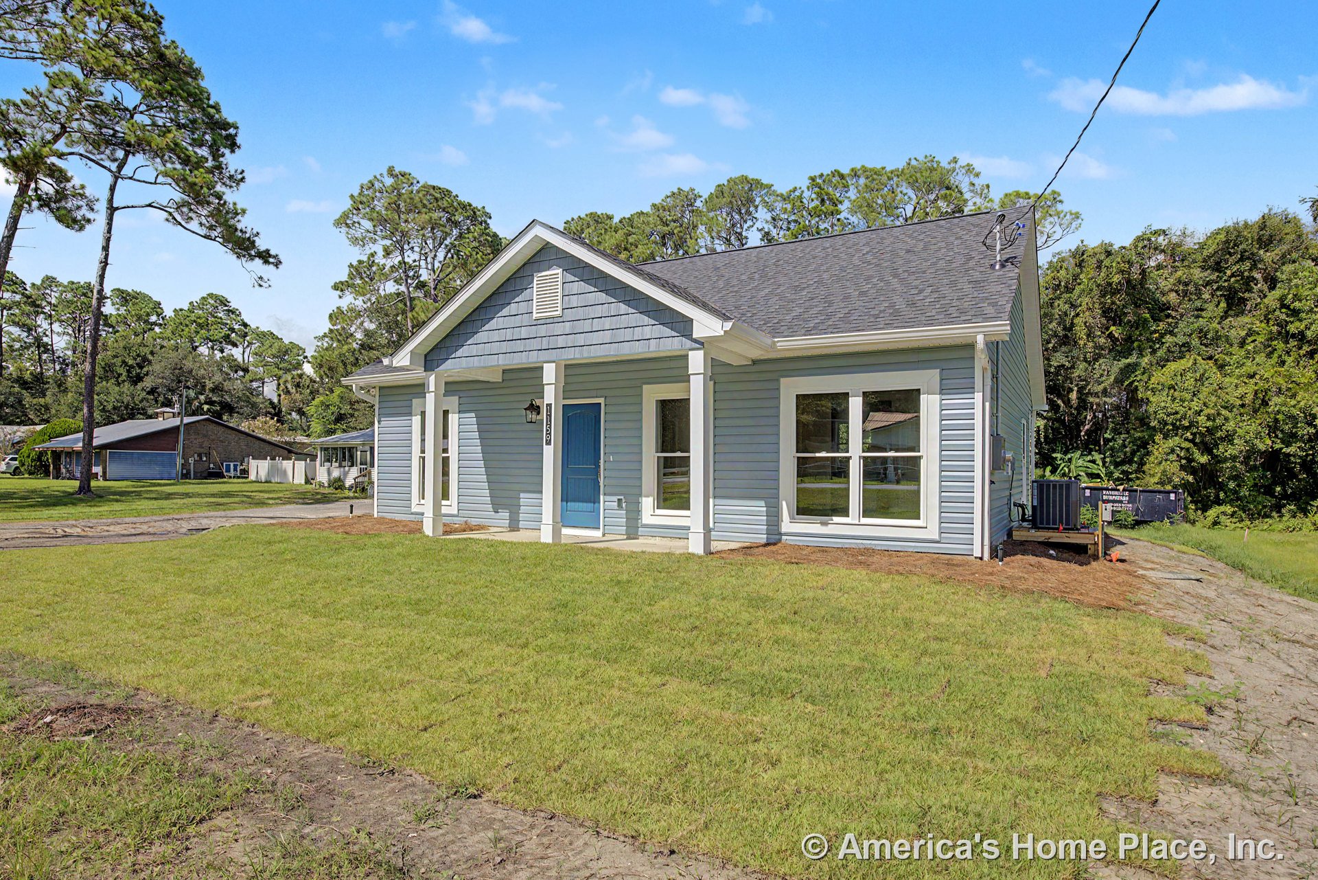 Covered front porch with white columns, blue entry door, large double-pane windows, lap siding exterior, gable roof, exterior wall lantern, and decorative trim.