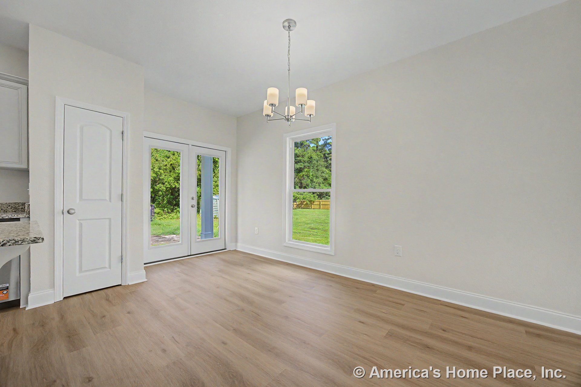 Dining area with light wood plank flooring, white trim and baseboards, double glass patio doors, single large window, modern ceiling chandelier, and neutral wall color in an open