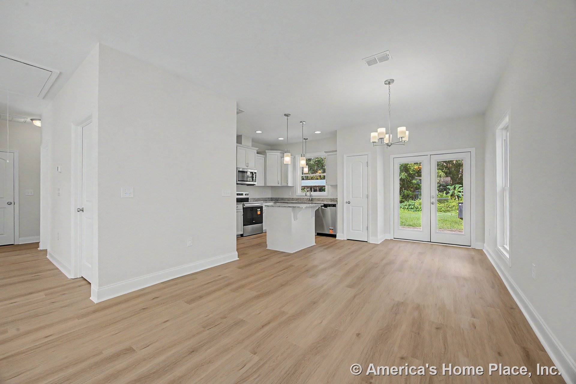 Open kitchen and dining area with white shaker cabinets, granite kitchen island, stainless steel appliances, pendant and chandelier lighting, double glass patio doors, and light