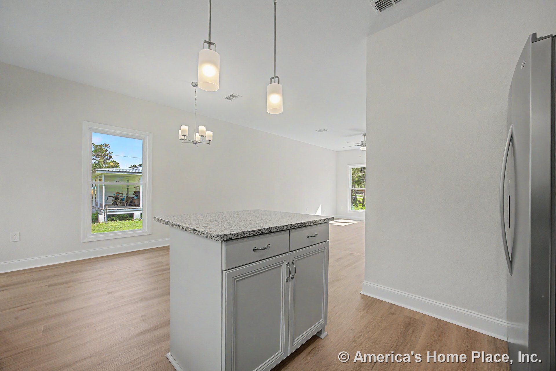 Granite kitchen island with pendant lights, light wood flooring, white cabinetry and trim, large windows, stainless refrigerator, recessed ceiling, and open layout.