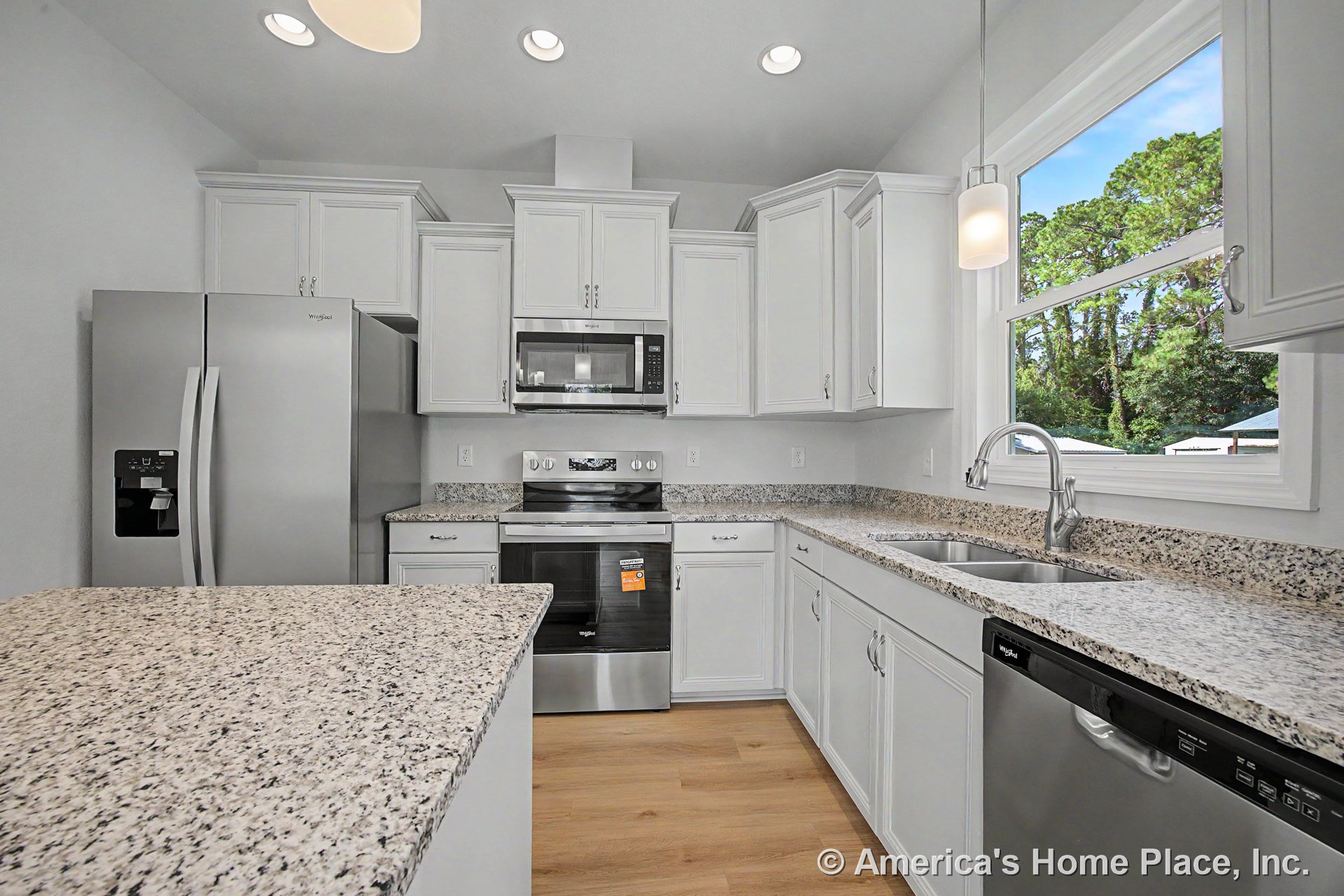 Granite peninsula with double bowl undermount sink, stainless steel refrigerator, electric range, microwave, and dishwasher; white upper and lower cabinets; recessed ceiling