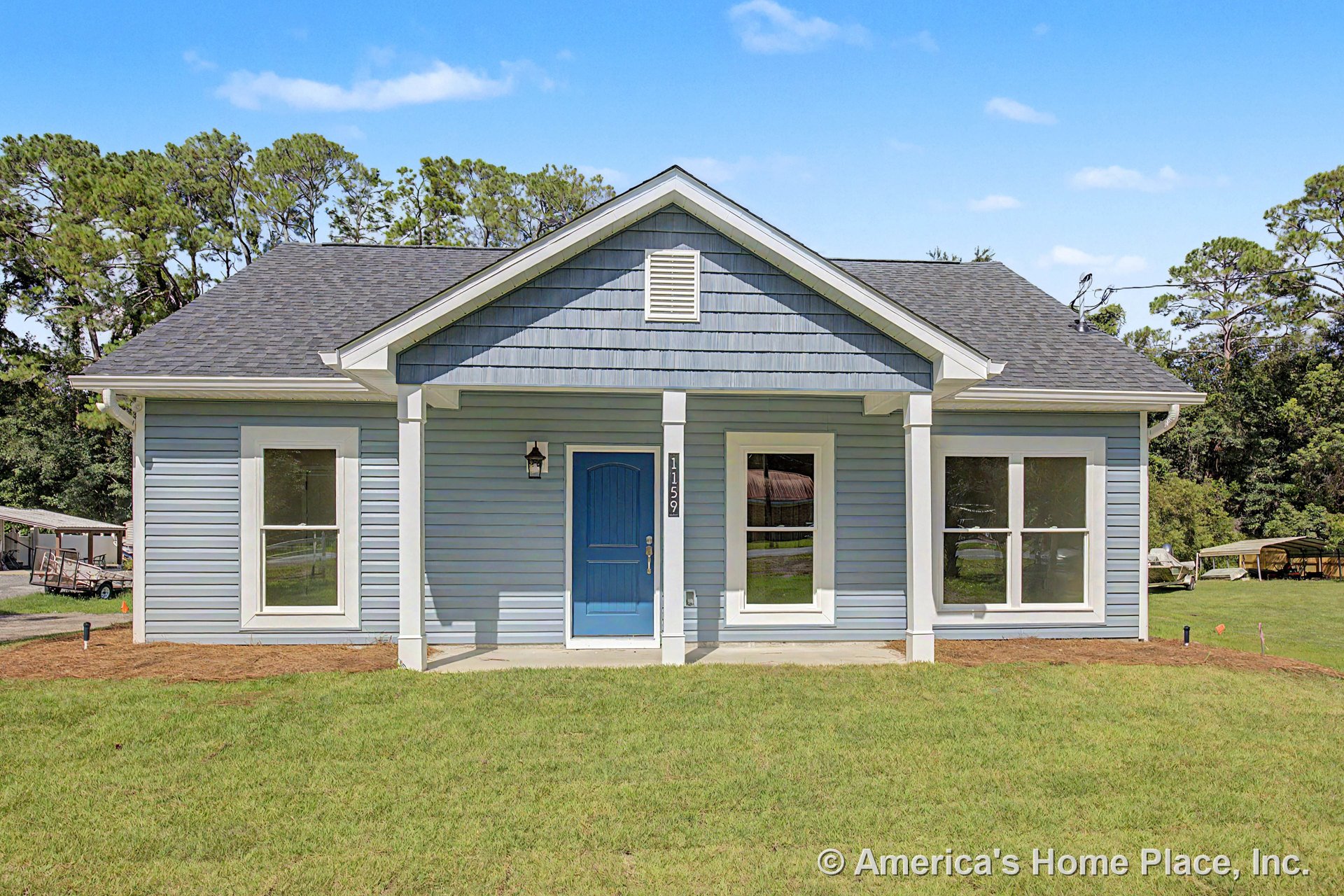 Blue siding exterior with white trim, double-hung windows, gable shingle roof, covered front porch featuring a blue entry door, exterior wall-mounted light fixture, and attic vent.