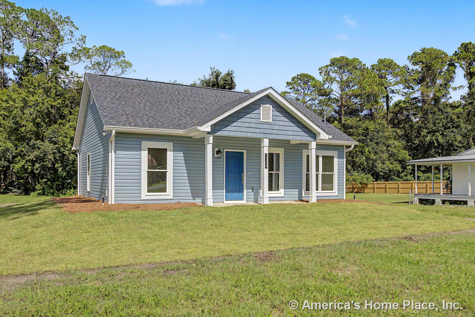 Blue exterior siding with white window trim, covered front porch supported by columns, front entry door, architectural roof shingles, and outdoor lighting fixture.