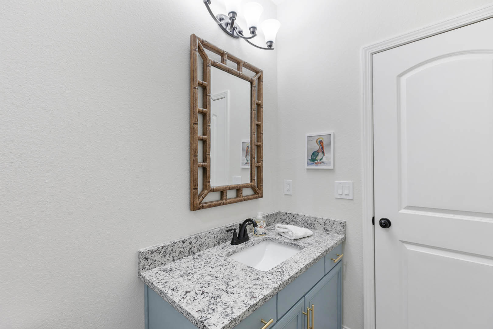 Bathroom with white countertop and sink, rectangular mirror above, towel folded on counter, bird painting on wall, ladder leaning against mirror, close-up of white door and modern