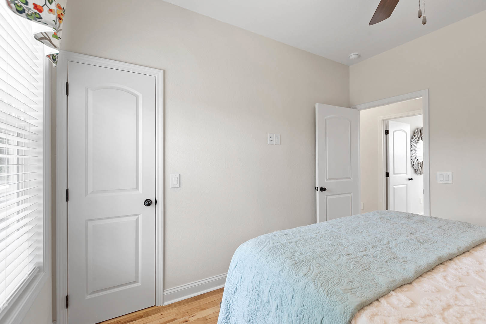 Bedroom with white walls, blue bedspread, white door featuring black hardware, window with white blinds