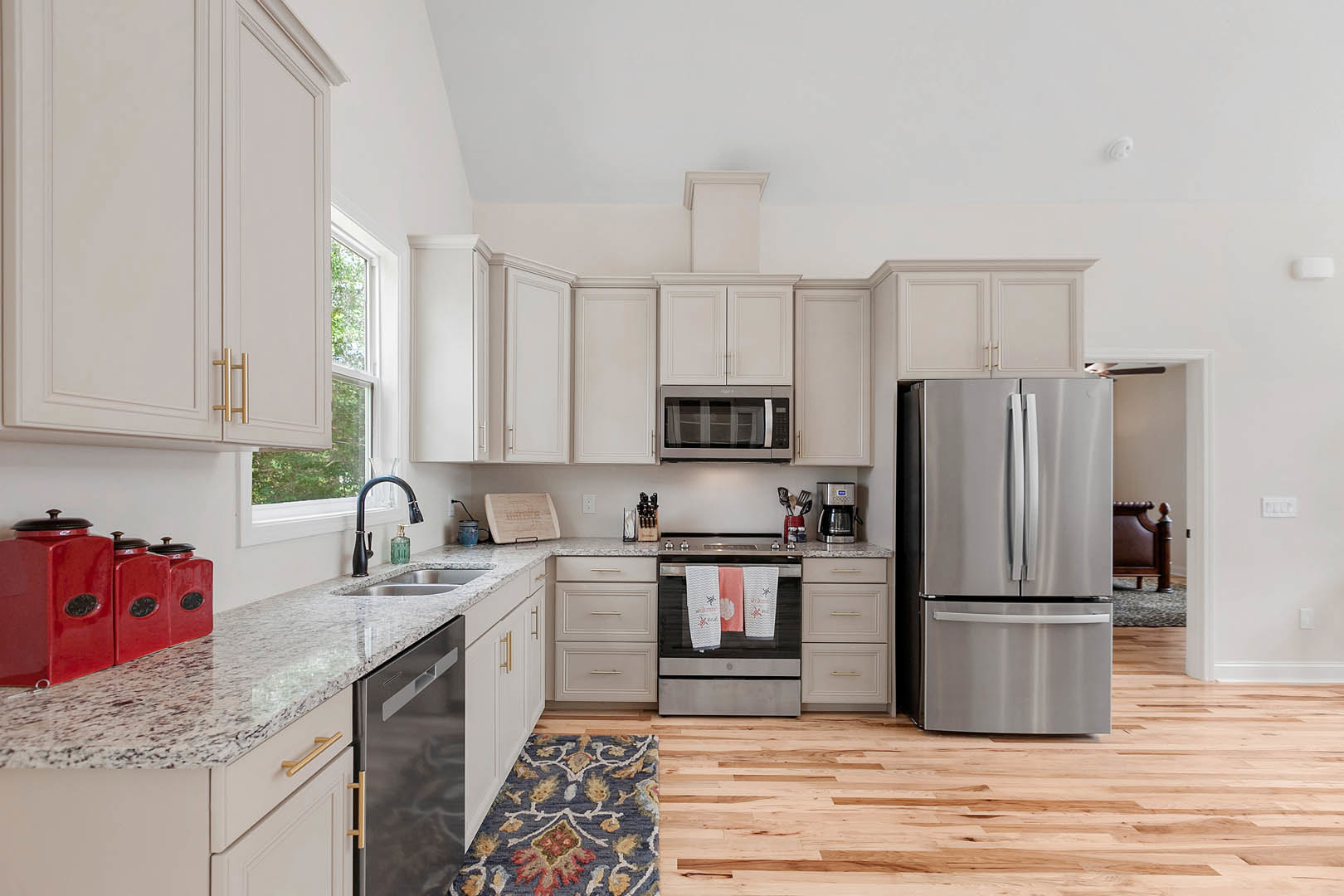 White kitchen cabinets and marble flooring, double-door silver refrigerator, microwave with glass window, towels hanging on oven, patterned rug on floor, close-up of glass door.