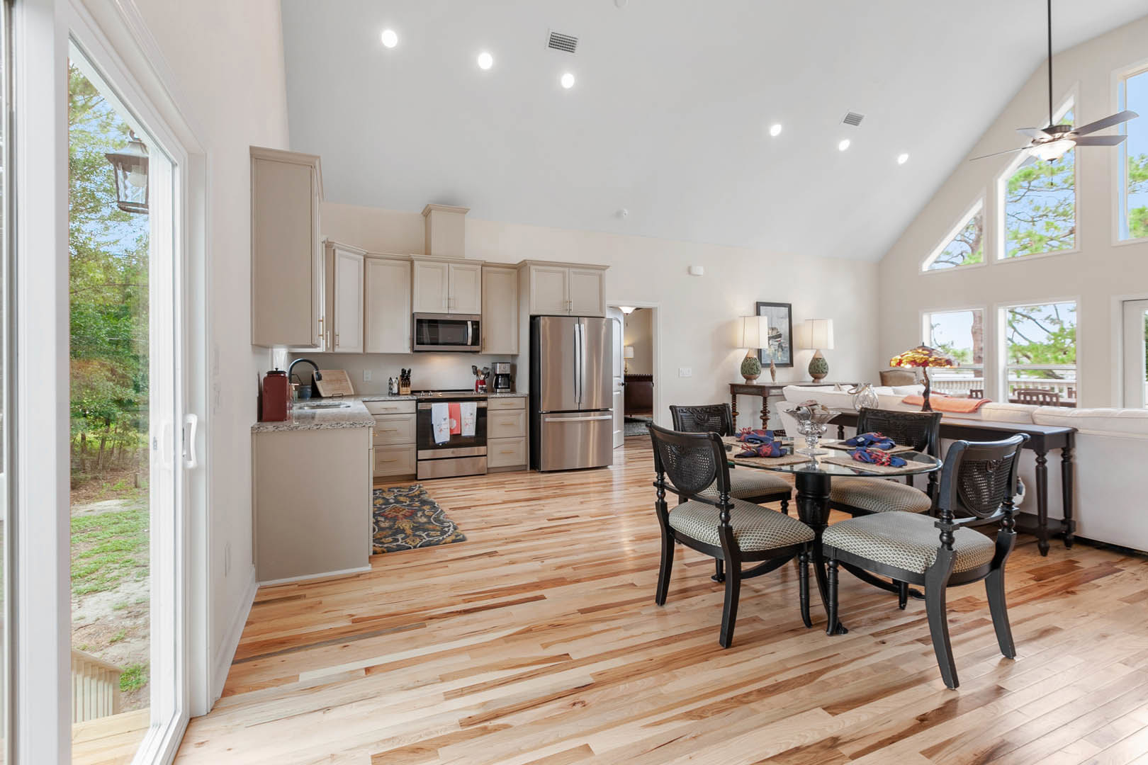 Open-concept kitchen and dining area featuring wood cabinetry, stainless steel refrigerator, glass-topped dining table with upholstered chairs, laminate flooring, and a built-in