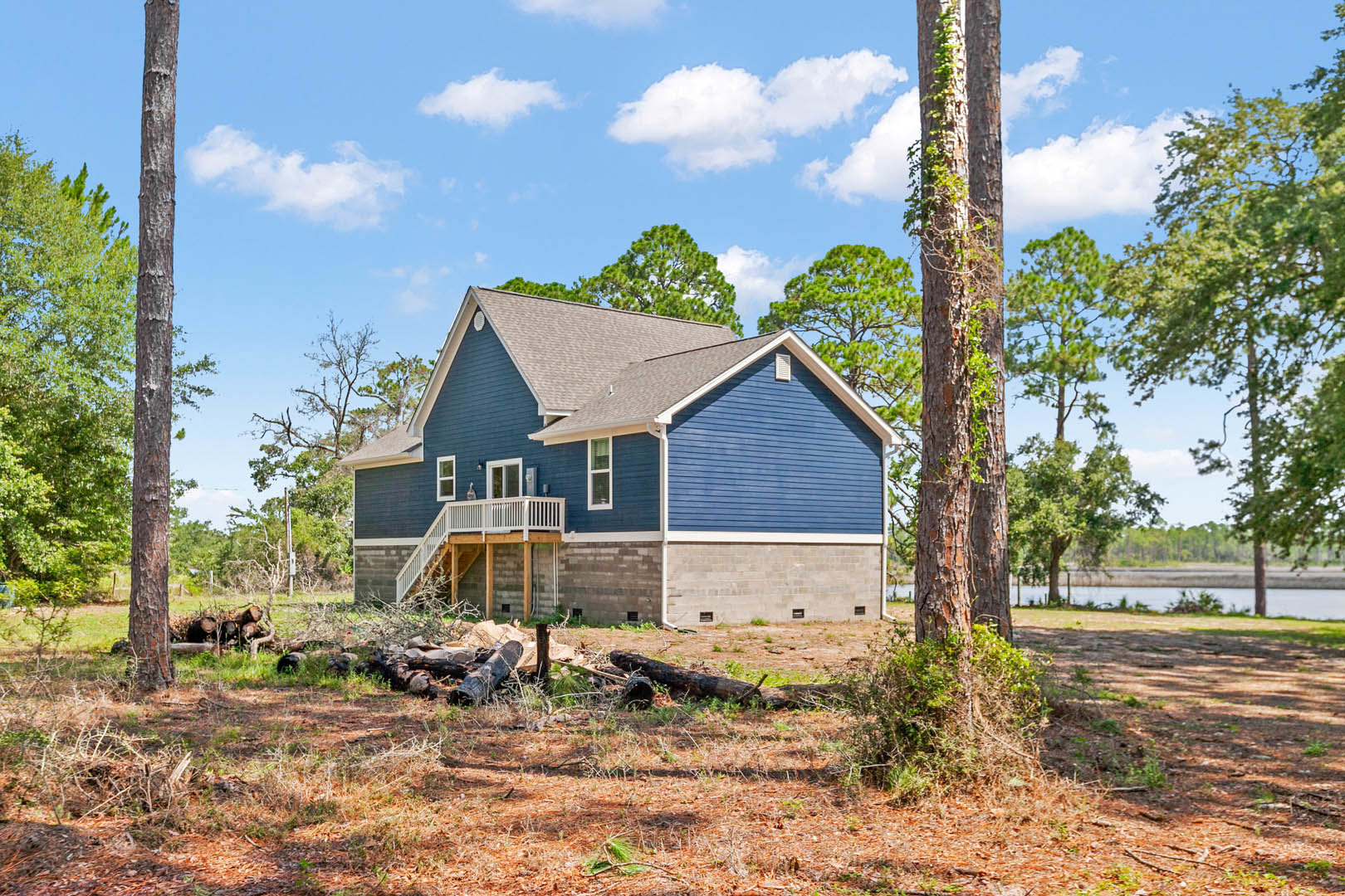 Blue siding house with white roof, wooden deck, grassy yard, tree stump in foreground, leafy tree and cloudy sky in background