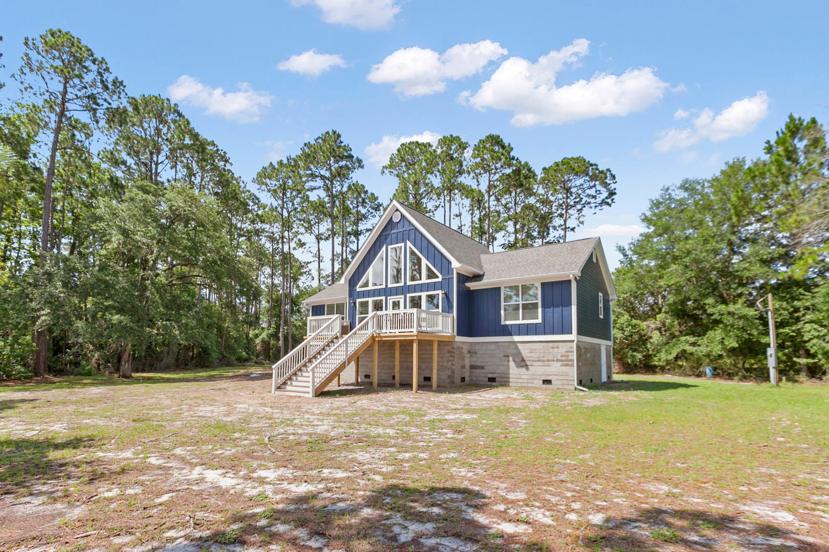 Blue siding house with white porch and stairs, surrounded by green grass and mature trees under partly cloudy sky