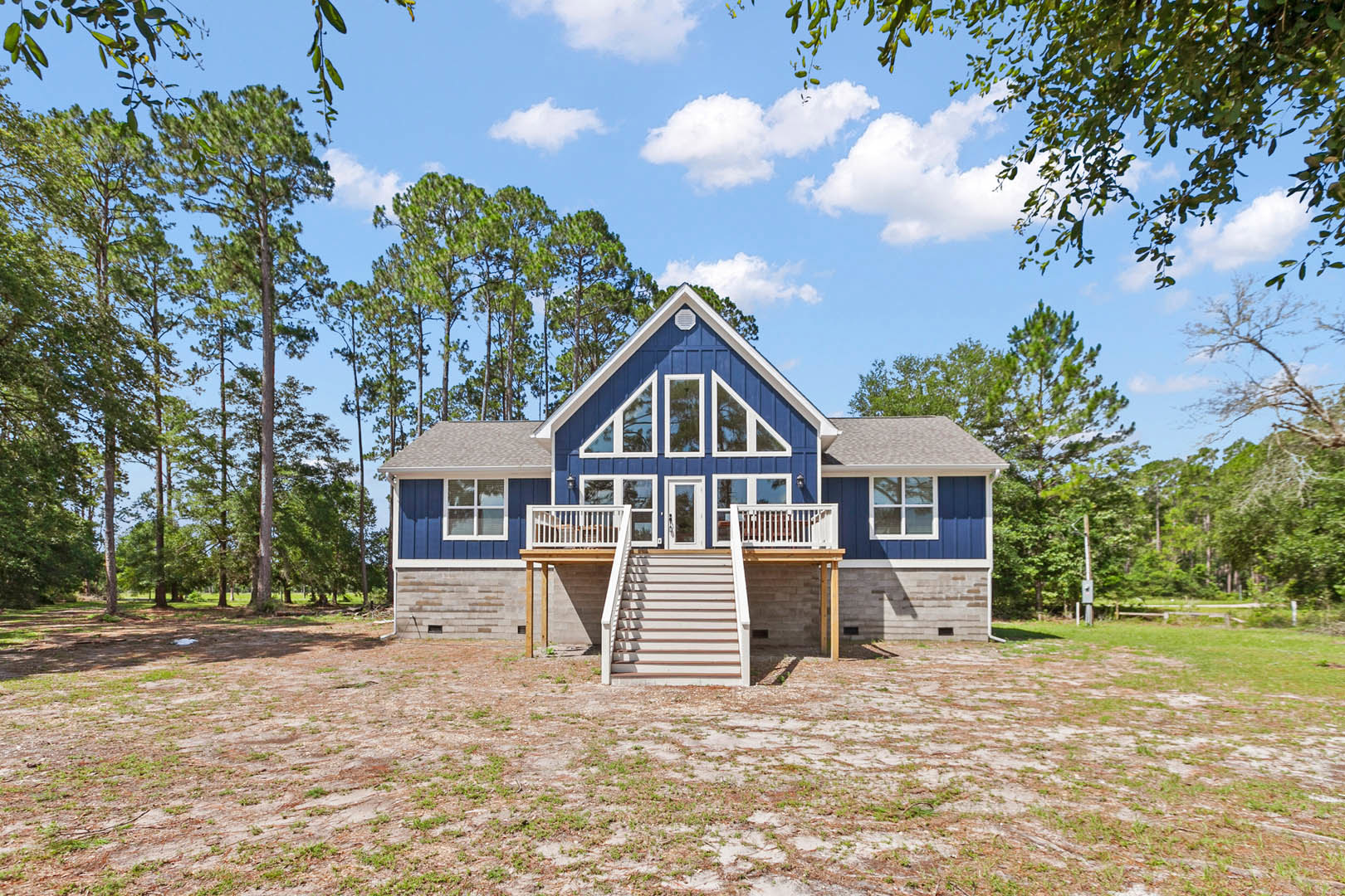 Blue siding house with white trim, front porch, and white staircase, surrounded by grass and trees under a partly cloudy sky