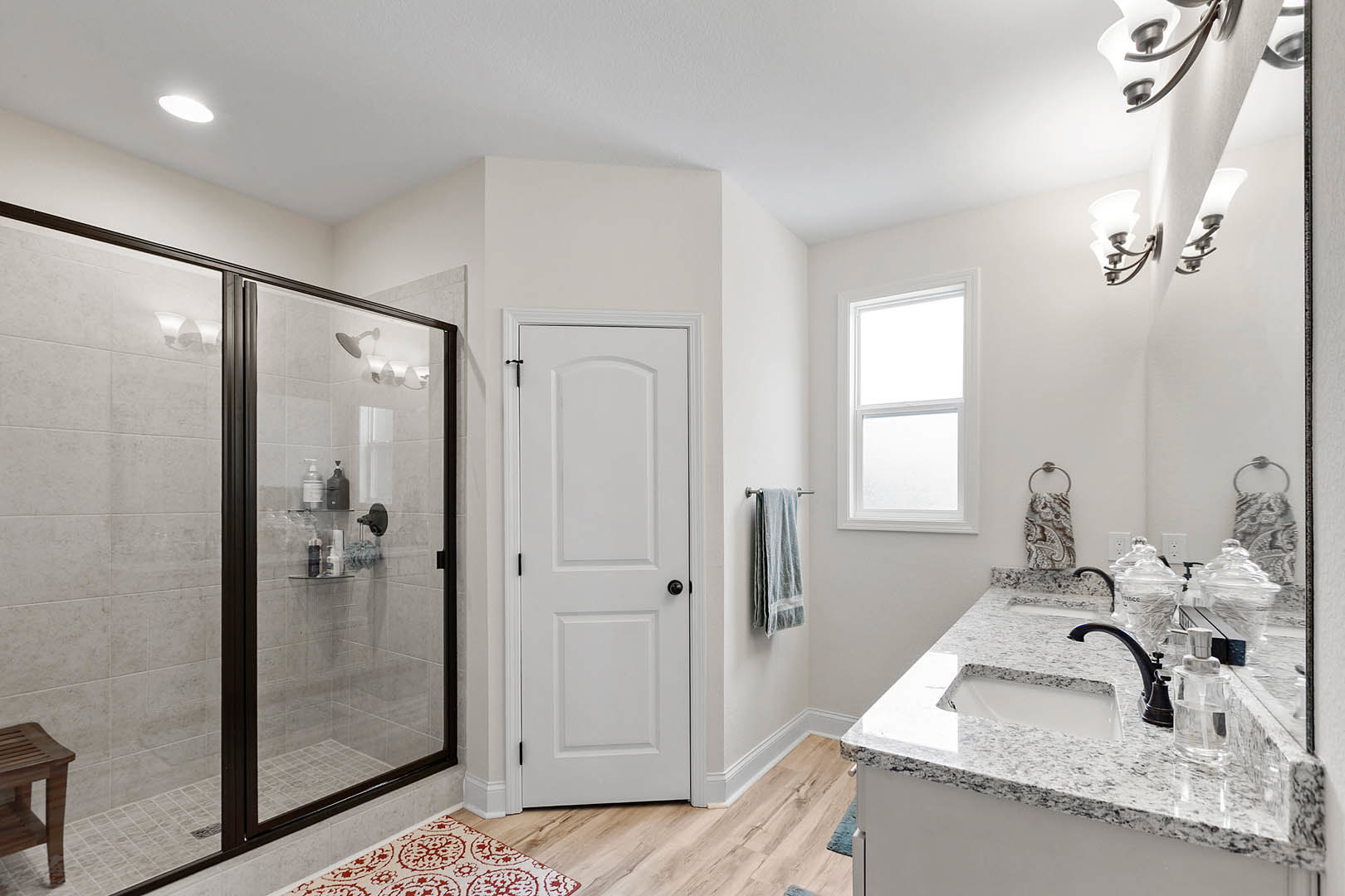 Bathroom featuring a glass shower enclosure, white sink with chrome faucet, white door with black knob, light tile flooring, and a neatly folded towel on the countertop.