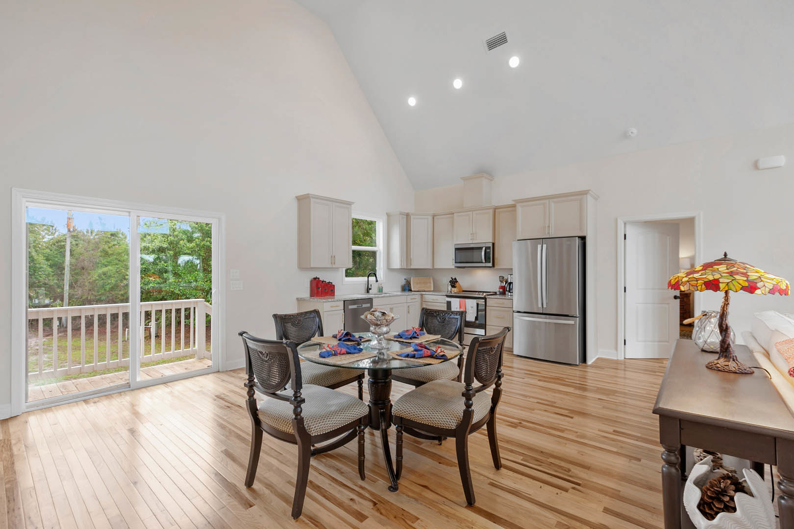 Open-concept kitchen and dining area featuring wood flooring, a rectangular dining table with matching chairs, stainless steel refrigerator, sliding glass door with white railing