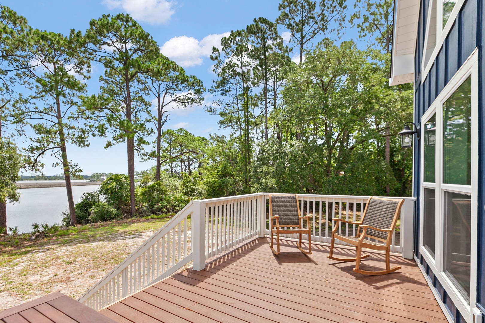 Wooden deck with two rocking chairs, white-framed window, railing, and leafy trees in the background