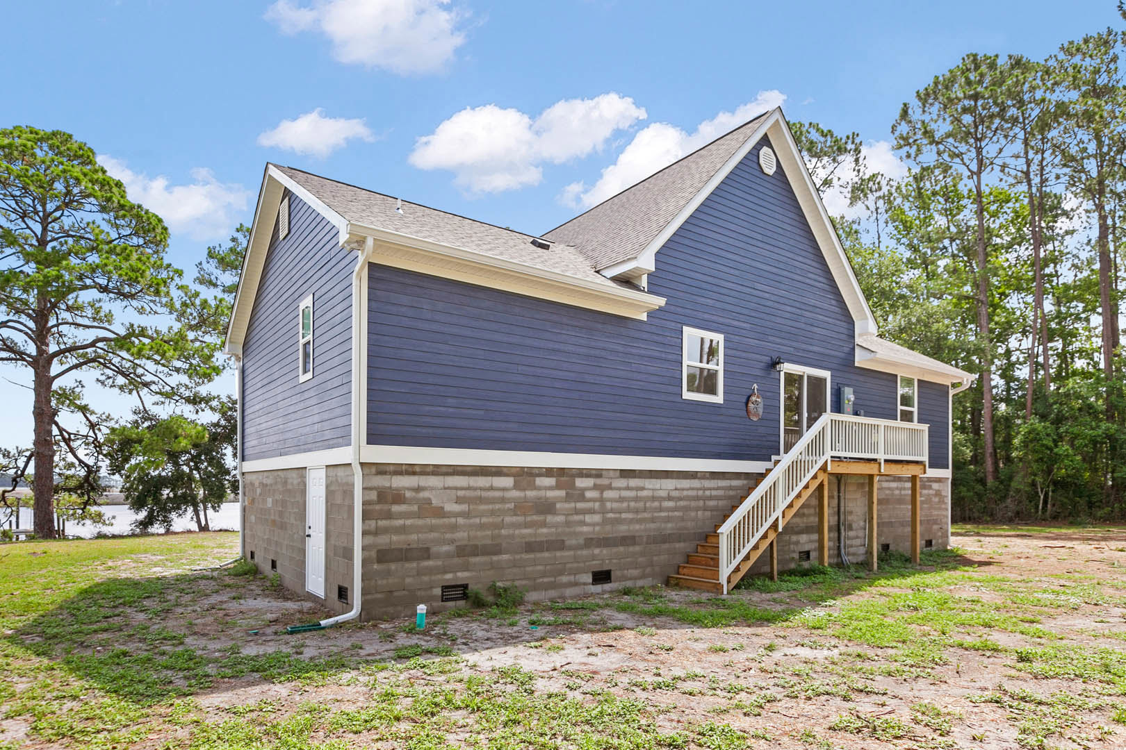 Two-story brick house with white-trimmed windows, covered porch, wooden staircase with white railing, attached garage, green lawn, and leafy tree in front yard.