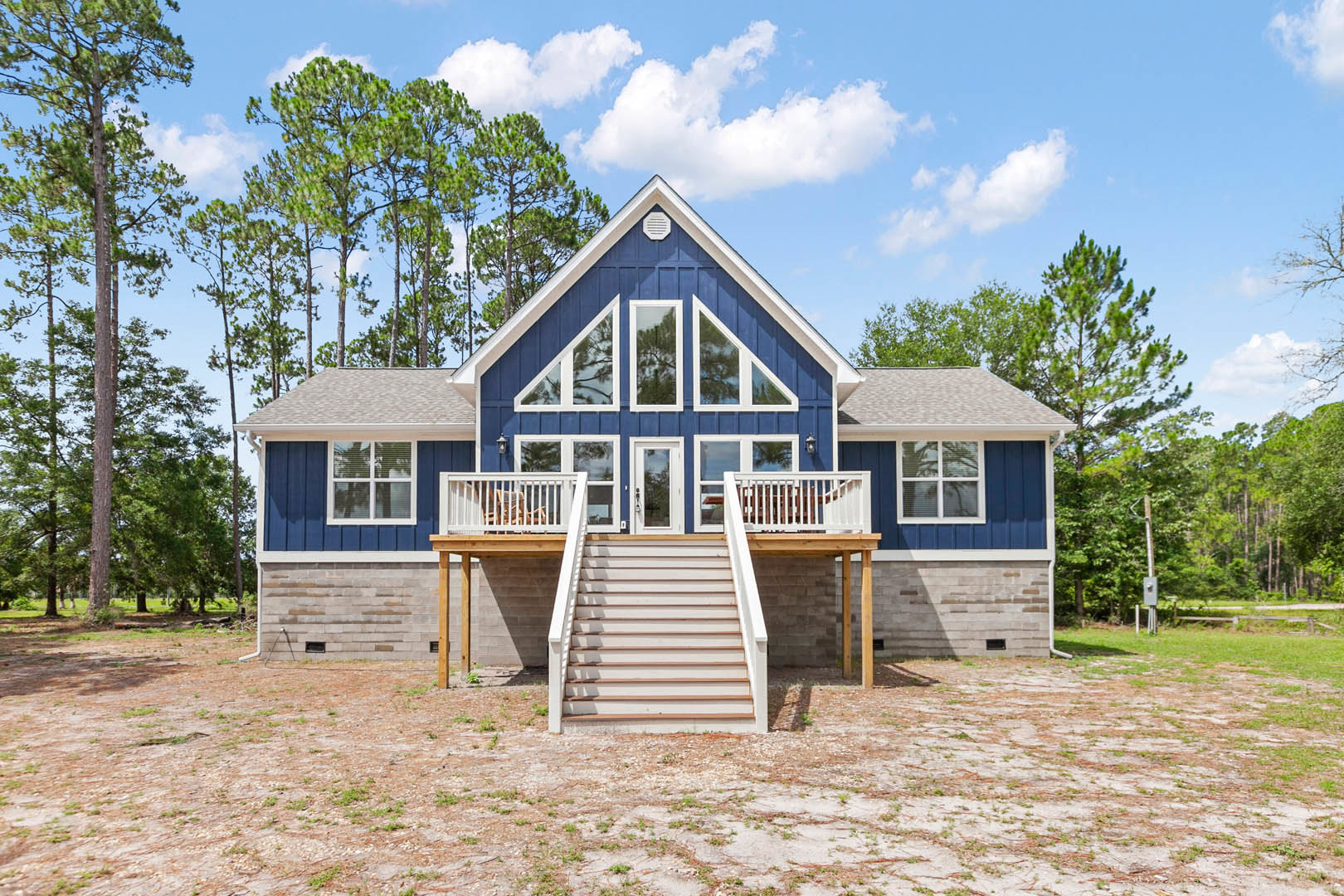 Blue house with white railings, blue roof, white-framed windows, and tree in foreground under clear sky