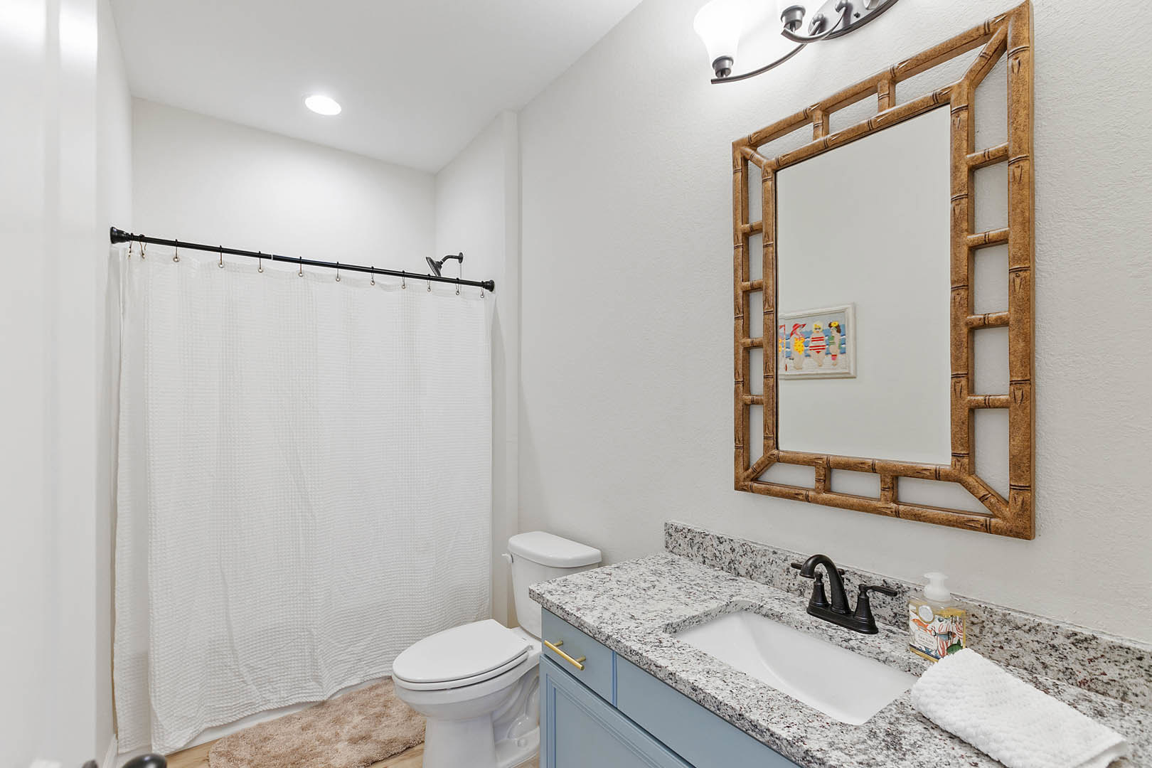 Bathroom with white tile walls, a wall-mounted mirror above a rectangular sink with a black faucet, a white toilet beside a tub with a white shower curtain, and a folded towel on