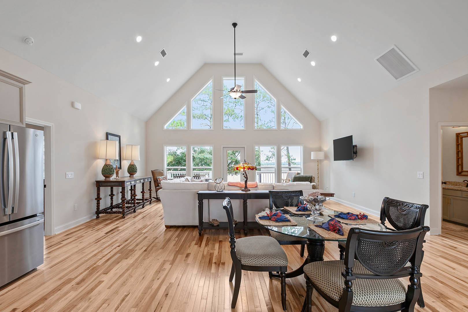Dining area with glass-top table, upholstered chairs, light laminate flooring, white cabinetry, stainless steel refrigerator, decorative vase centerpiece, and wall-mounted black