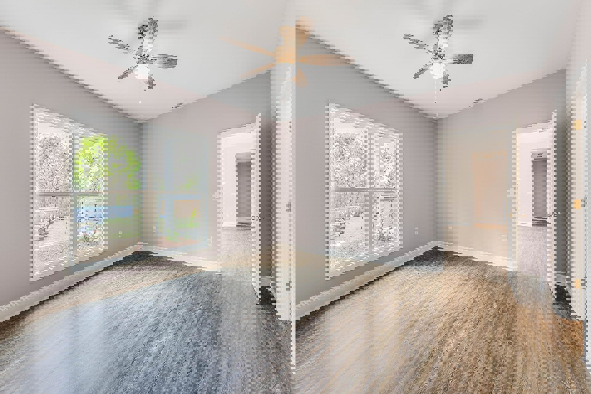 Ceiling fan with light fixture above wood laminate flooring, window overlooking green yard and trees, white plaster walls with crown molding