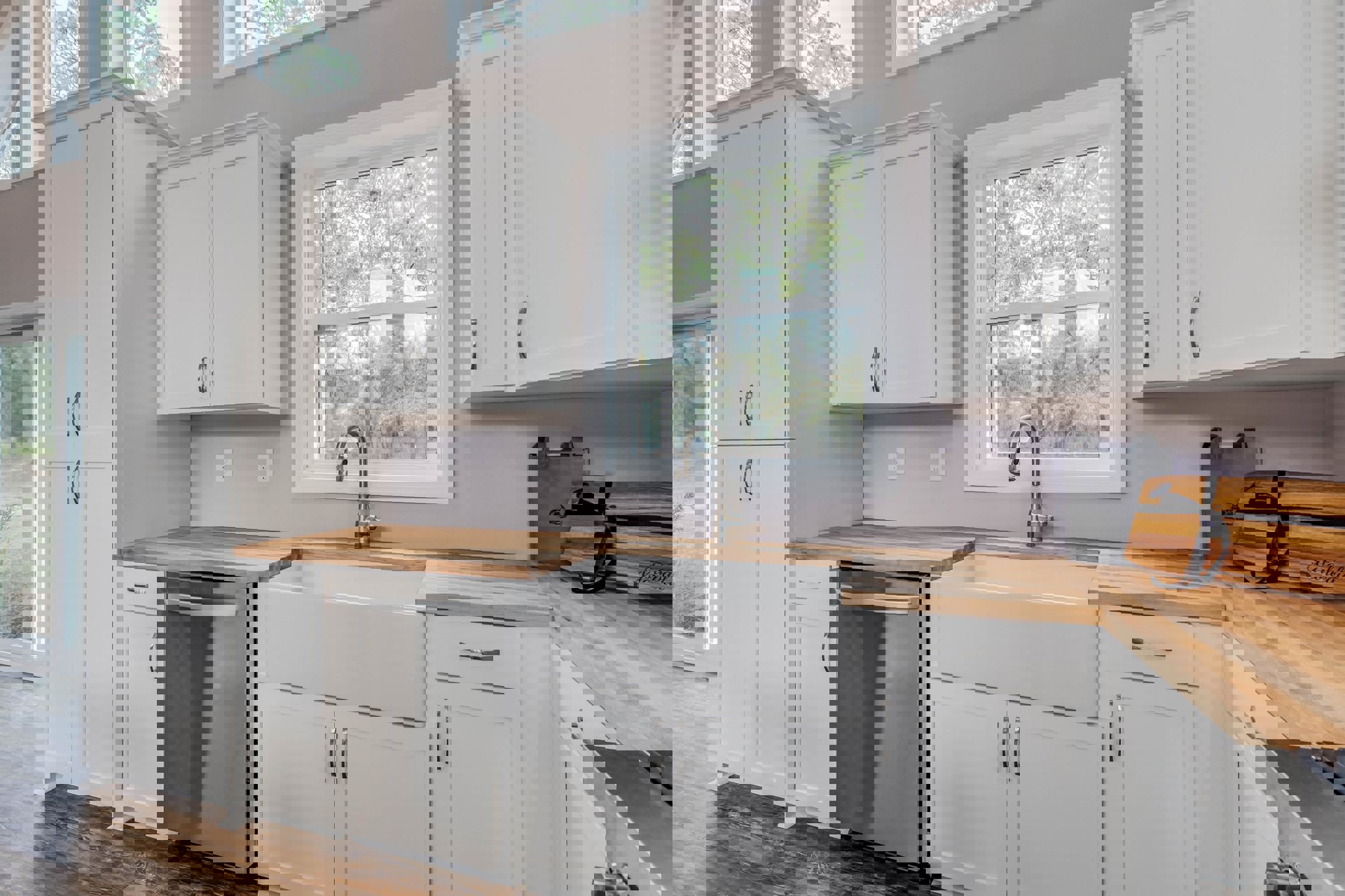 White kitchen cabinets with silver handles, stainless steel refrigerator, sink beneath a window overlooking trees, wooden box with black ribbon on countertop.