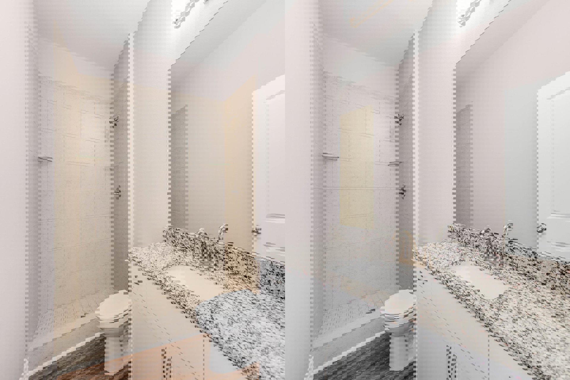 Bathroom with white toilet, bathtub shower with built-in shelves, white sink and faucet, wall-mounted mirror, light-colored tile flooring, and white paneled door