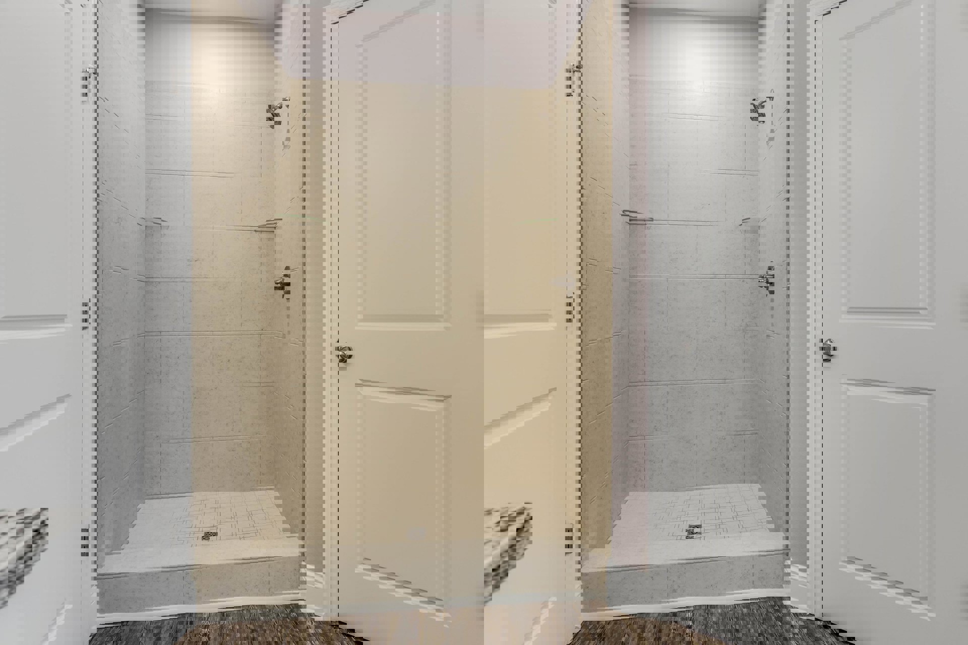 Walk-in shower with light gray tile floor, glass enclosure, white cabinet door with black trim, and white bathroom door featuring silver handle and visible hinge.