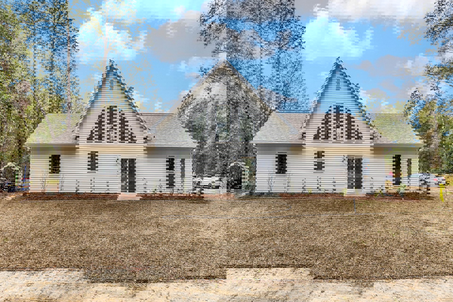 Two-story house with white siding, sliding glass door, illuminated window, front lawn with garden hose, mature trees, and parked car with black roof.