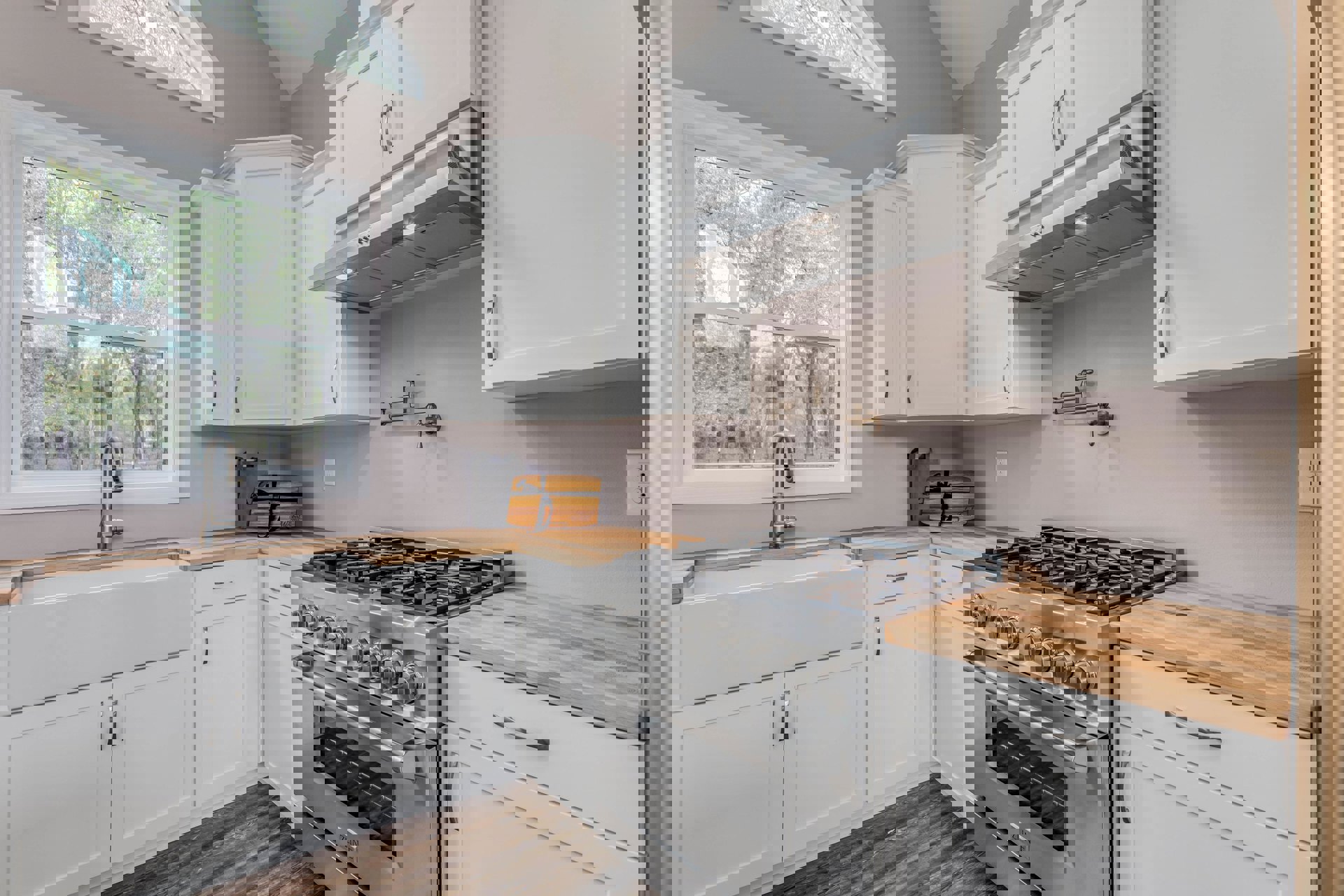 White kitchen cabinets with silver handles, stainless steel stove with glass door, sink and chrome faucet beneath a window, wooden box with black ribbon on countertop